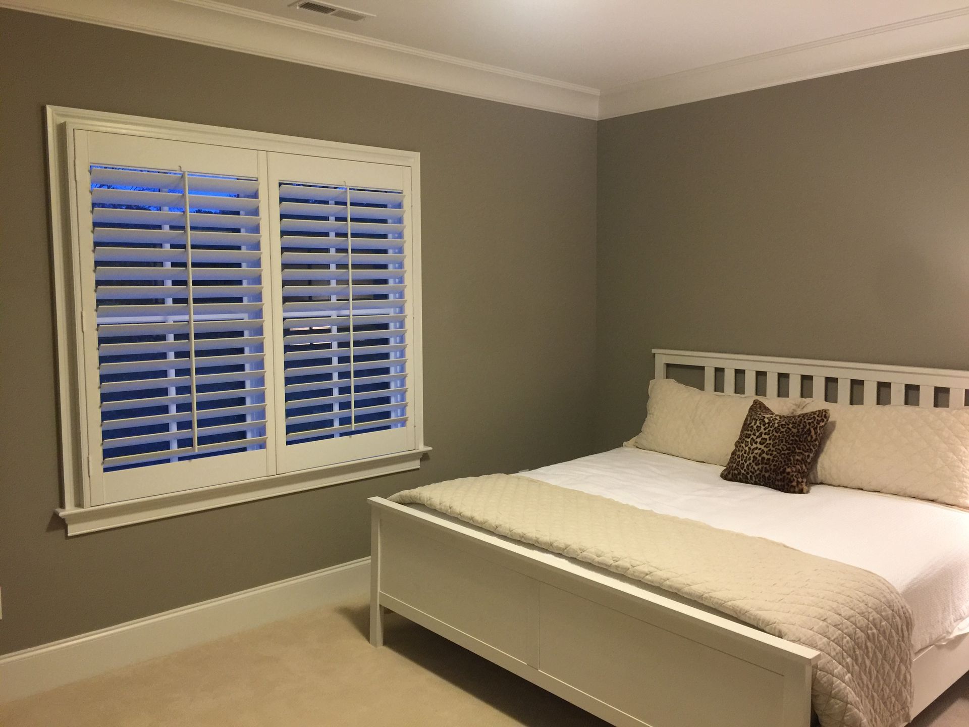 Bedroom with white bed, shutters, beige walls, and white trim.