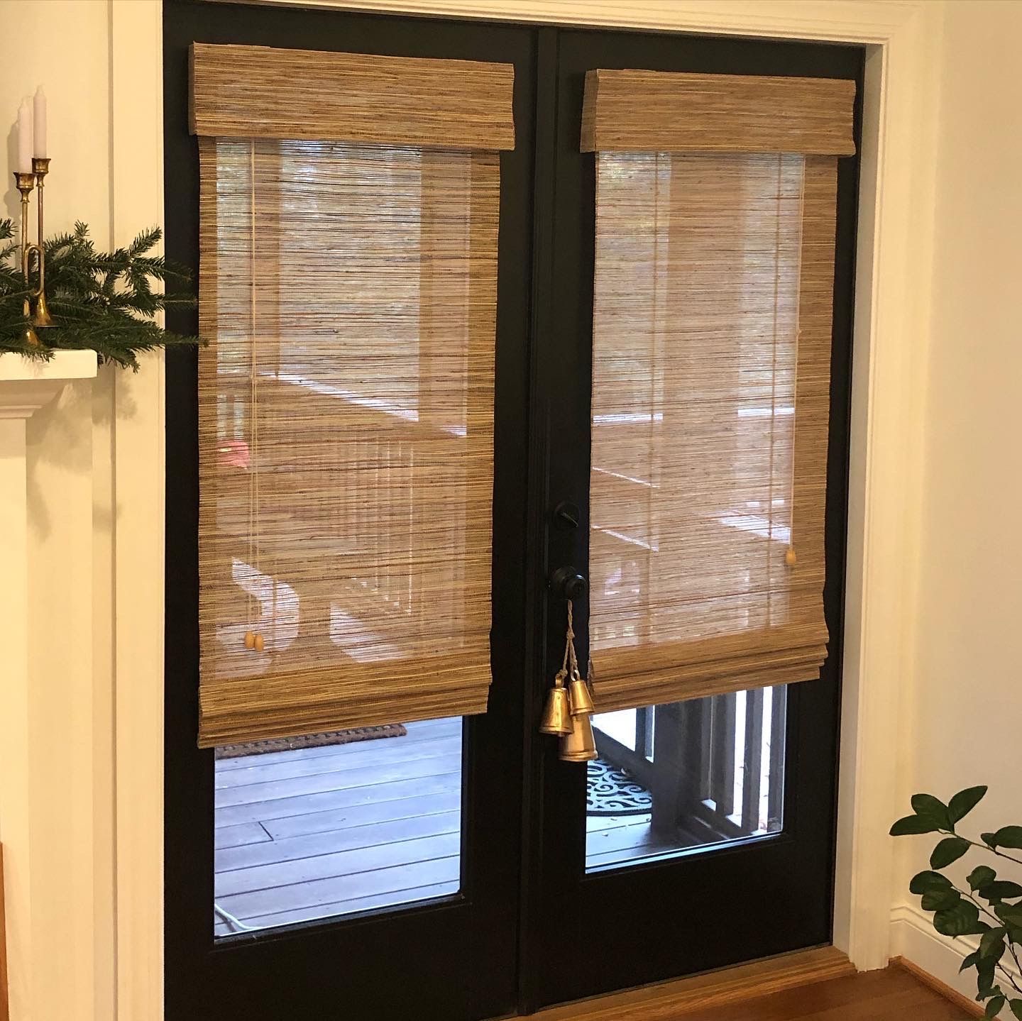Black French doors with woven shades, a light-colored interior, and a view of an outdoor space.