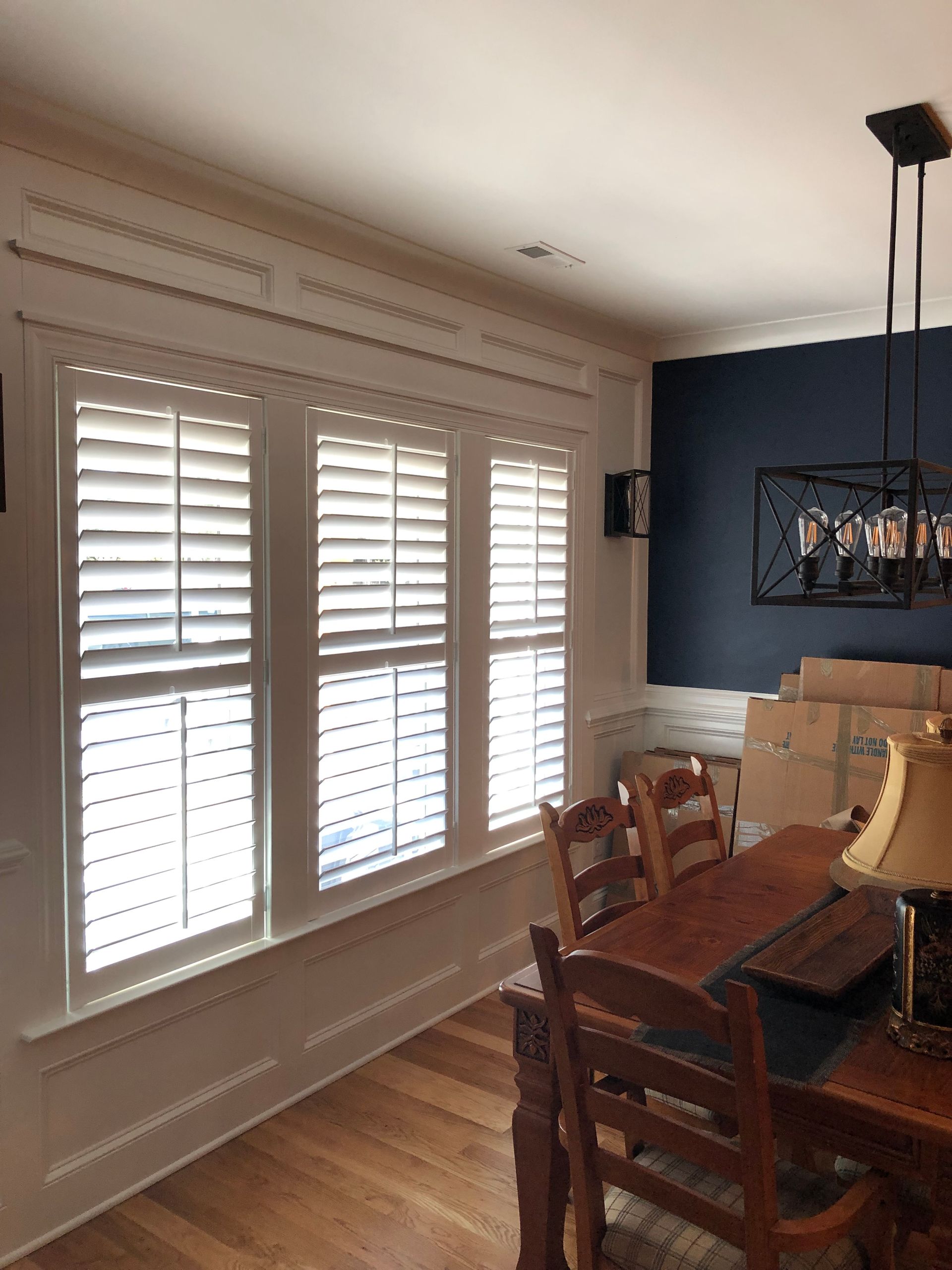 Dining room with wooden table, chairs, and shuttered windows. Navy blue accent wall.