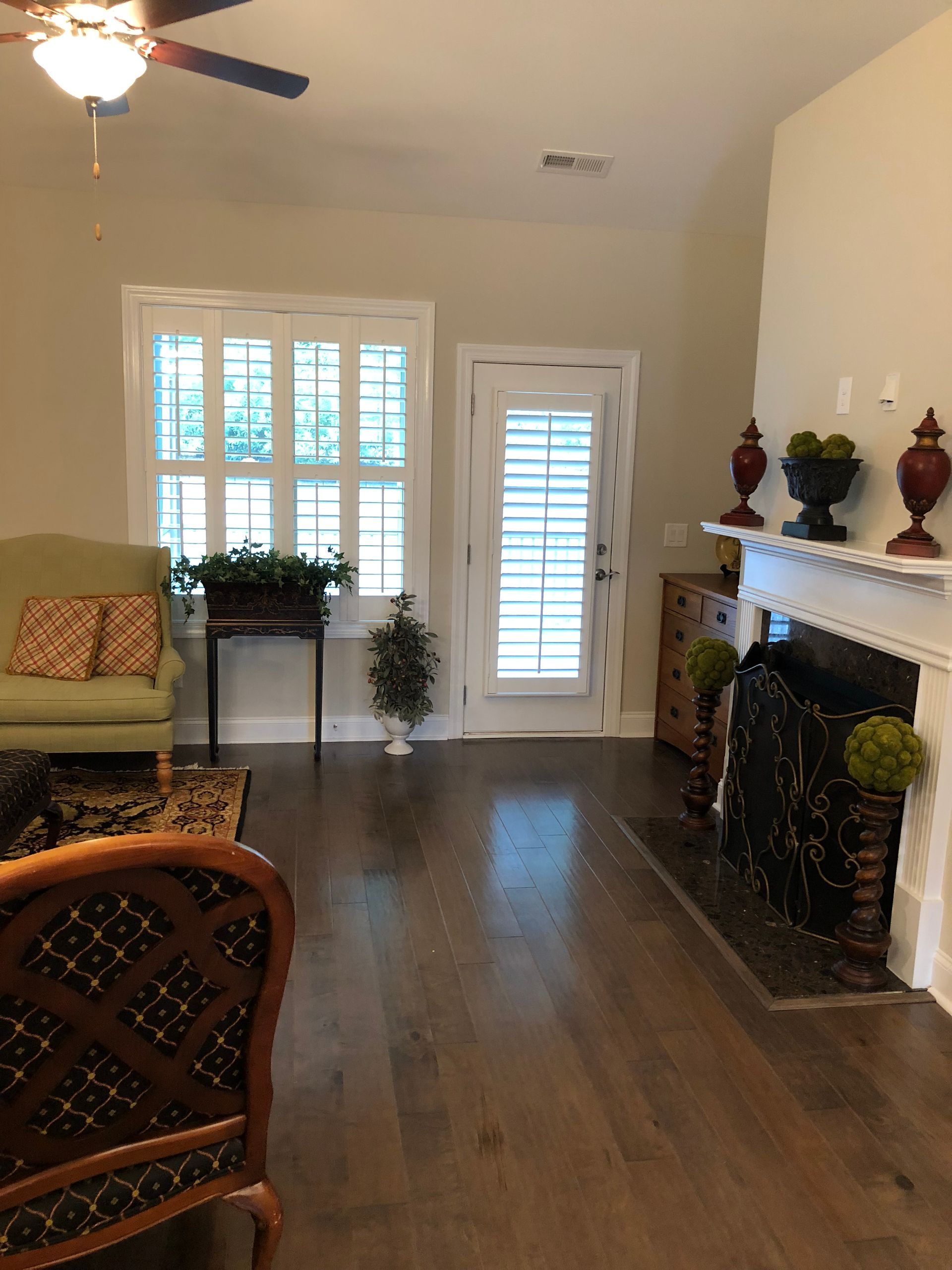 Living room with hardwood floors, fireplace, and green sofa. Window with shutters and a door with light coming in.