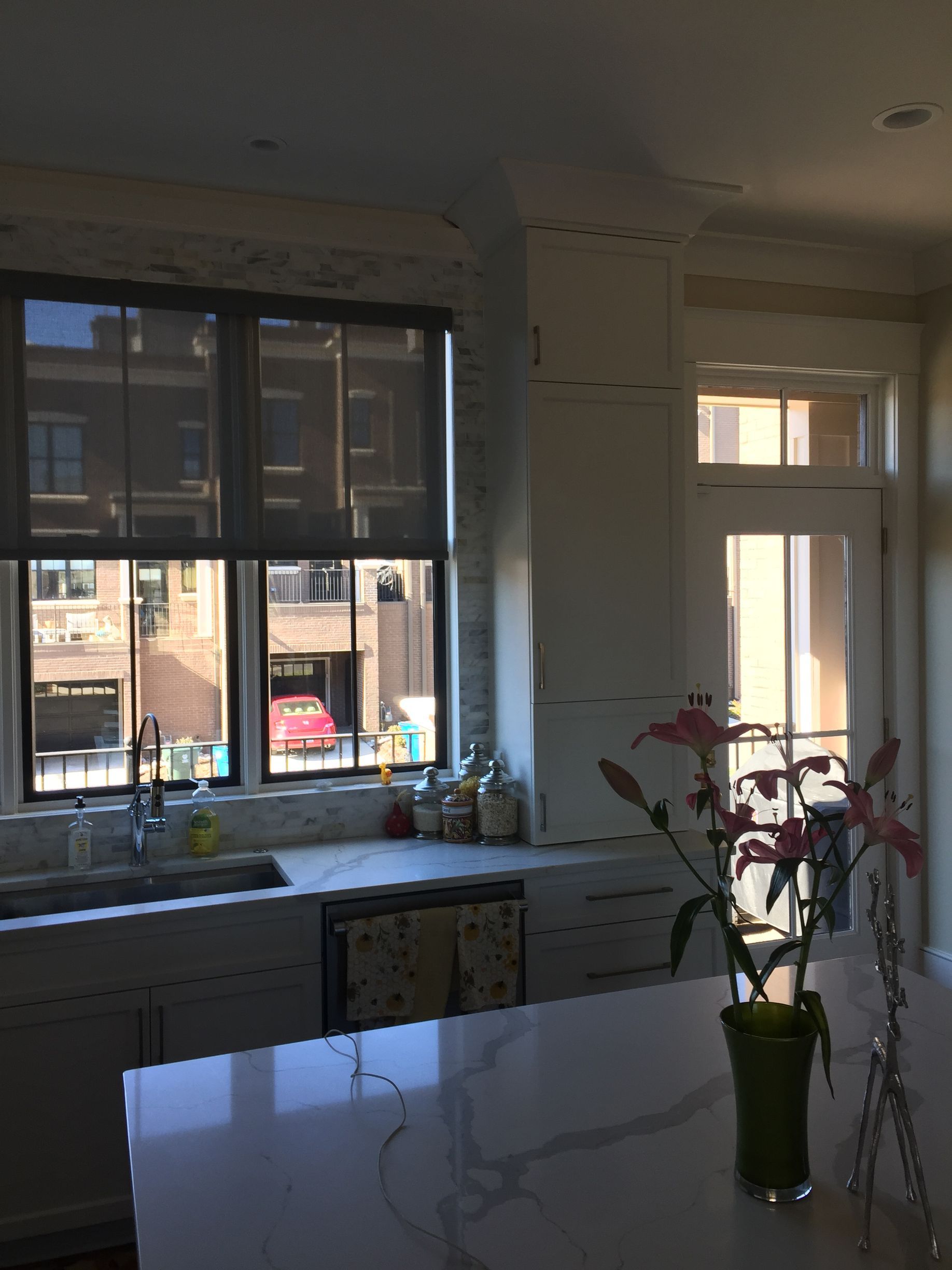Kitchen interior with window, white cabinets, island with marble countertop, and pink lilies.