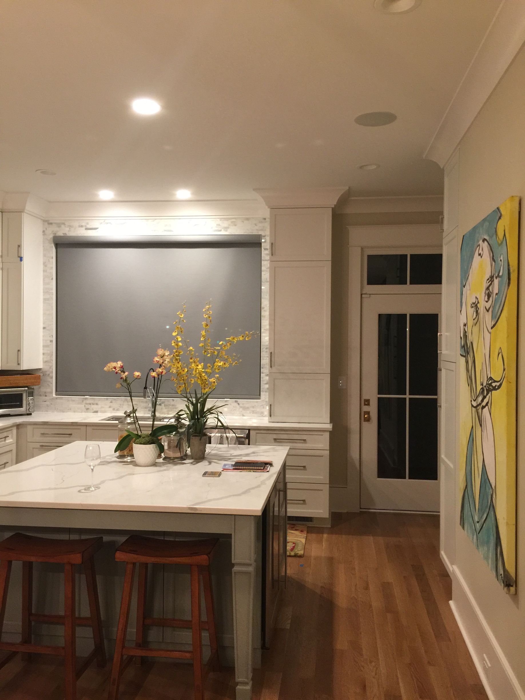 Kitchen with island, flowers, gray shade, and hallway with artwork.