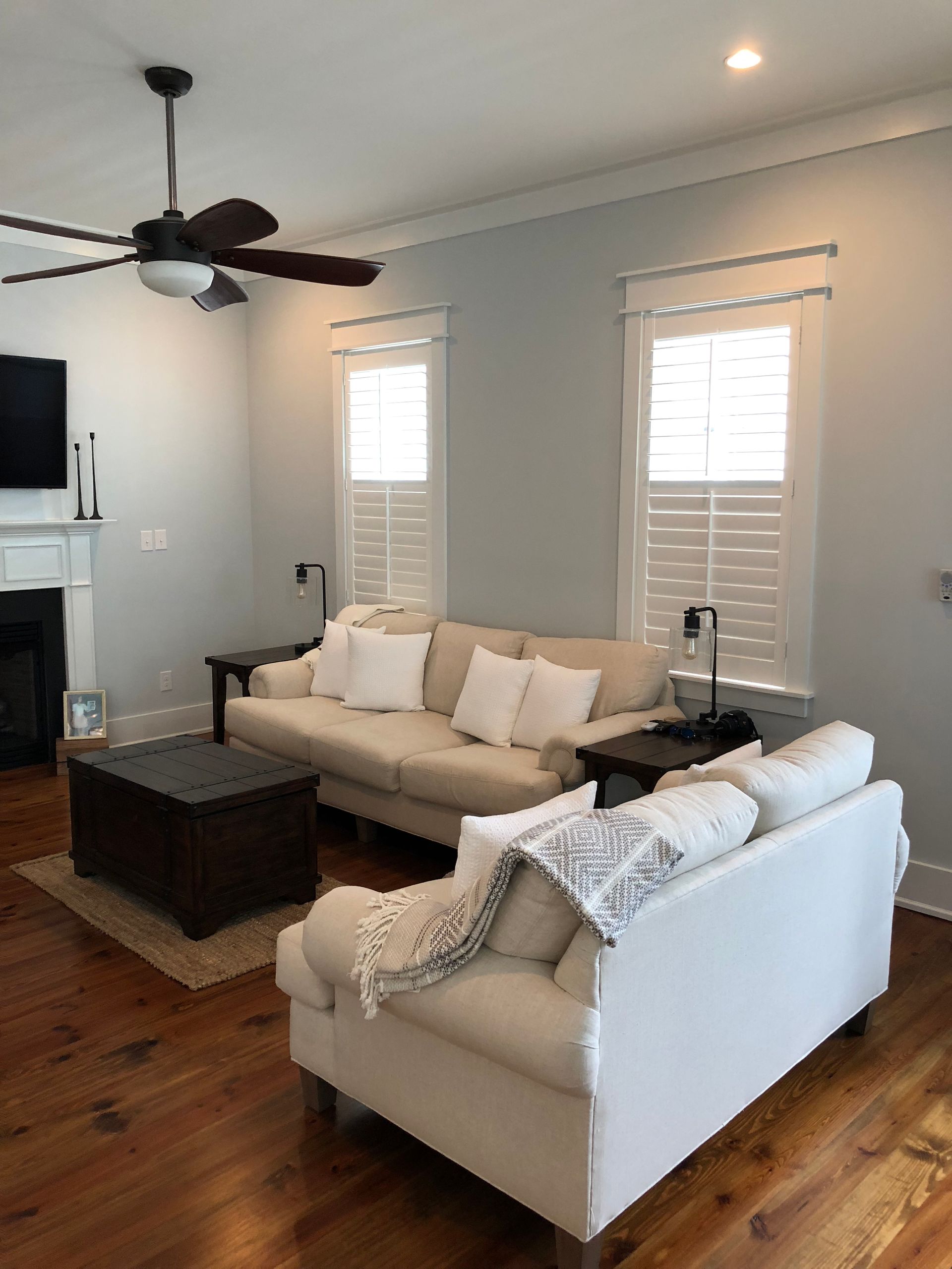 Living room with two white couches, dark wood coffee table, and windows with shutters.