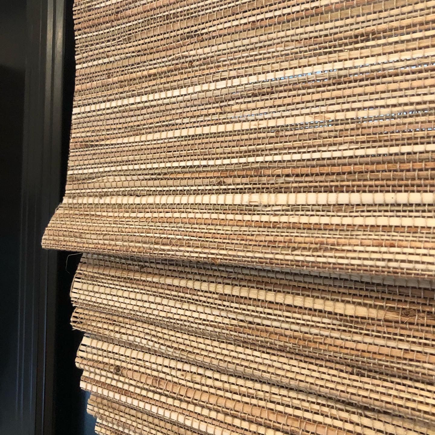 Close-up of woven natural fiber window shade, folded, against a dark wall.