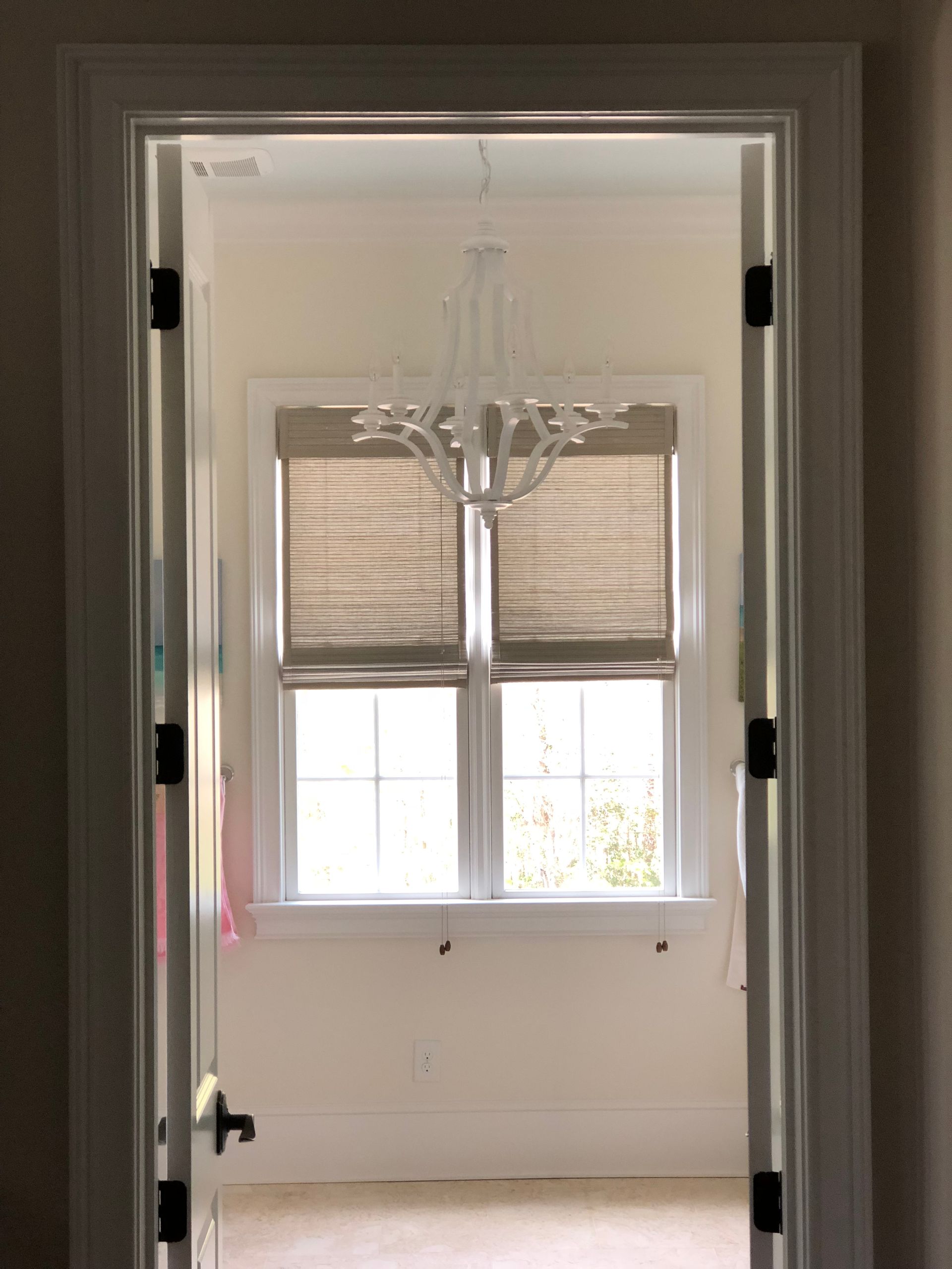 View through an open doorway of a room with a window, blinds, and a chandelier.