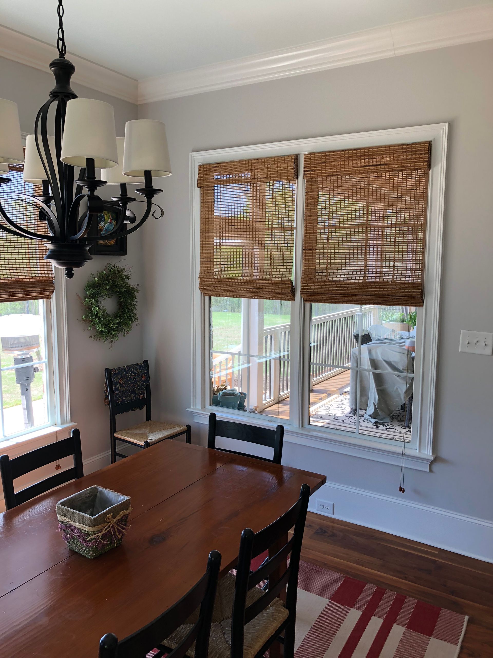 Dining room with wooden table, black chairs, woven blinds, and a chandelier.
