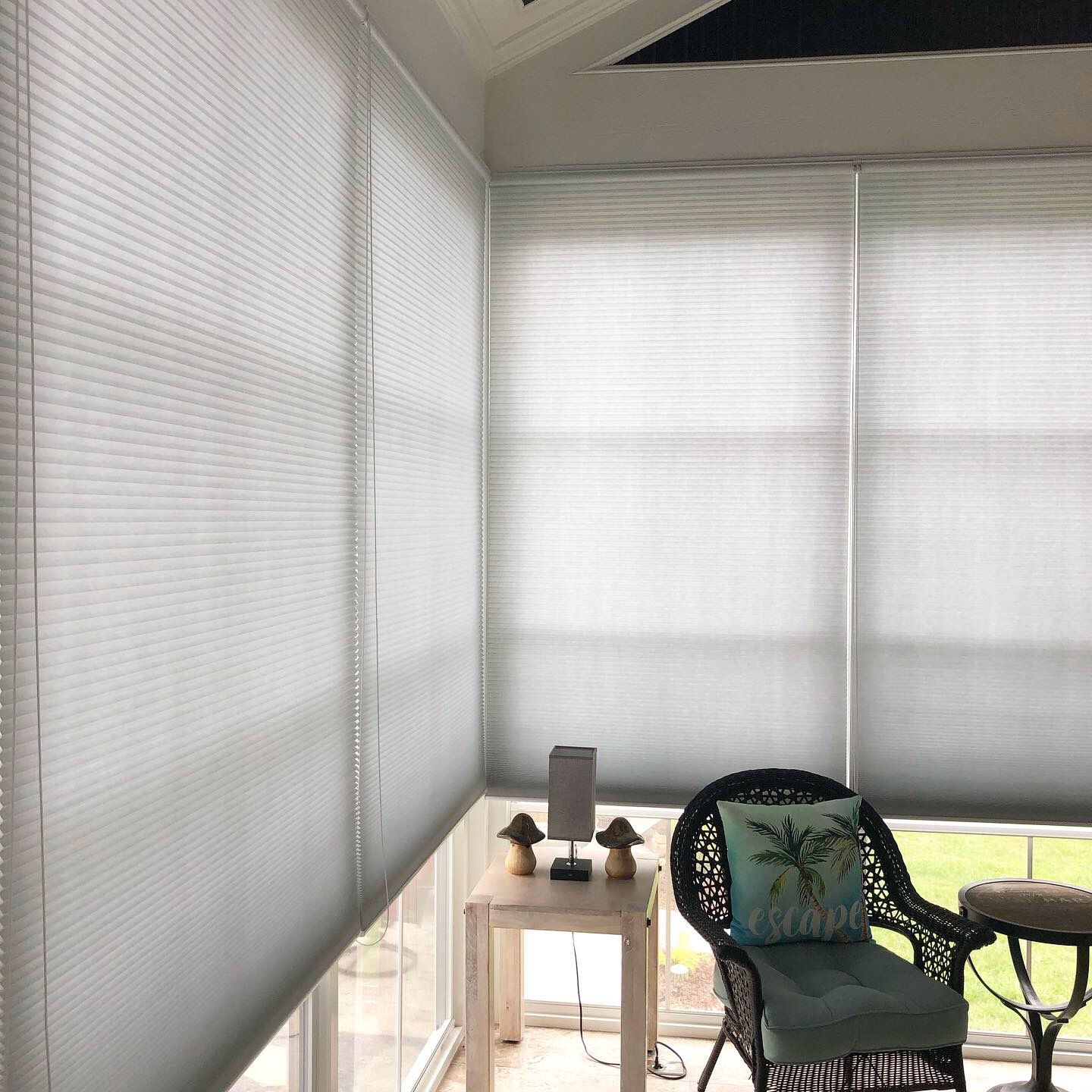 Sunroom with closed, light-colored honeycomb blinds on windows. A chair, table, and decorations are visible.
