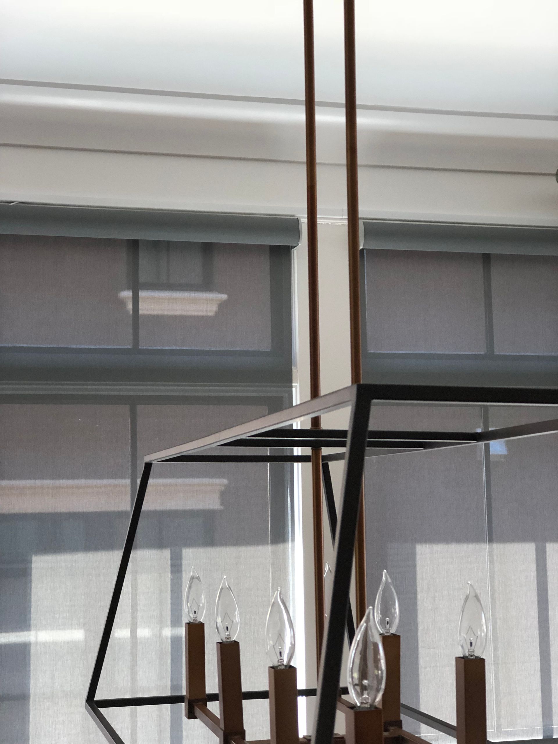 Close-up of a modern chandelier with exposed lightbulbs. Grey window shades and white ceiling visible.