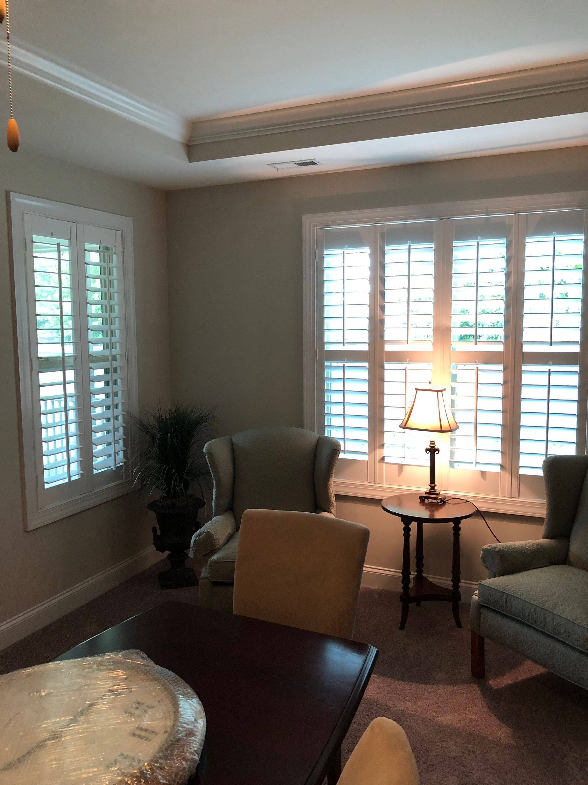 Interior room with white shuttered windows, armchairs, small table with lamp.