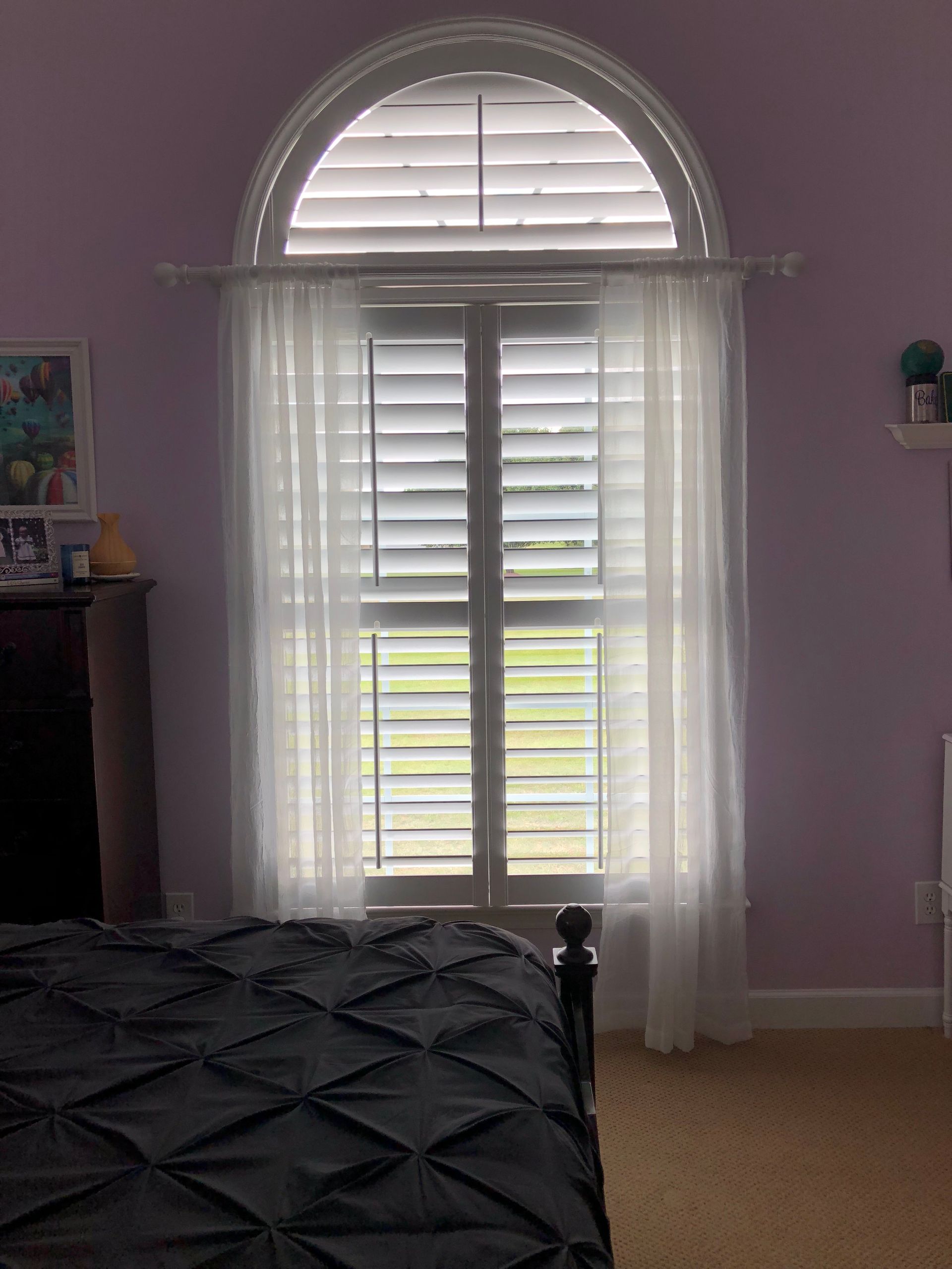 Window with white shutters and sheer curtains, in a room with a lilac wall.