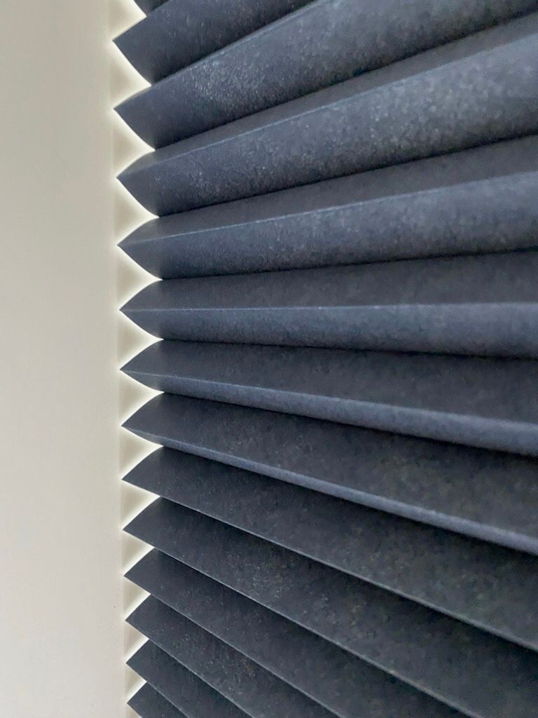 Dark blue pleated window blinds are partially open, casting a line of light along the adjacent white wall.