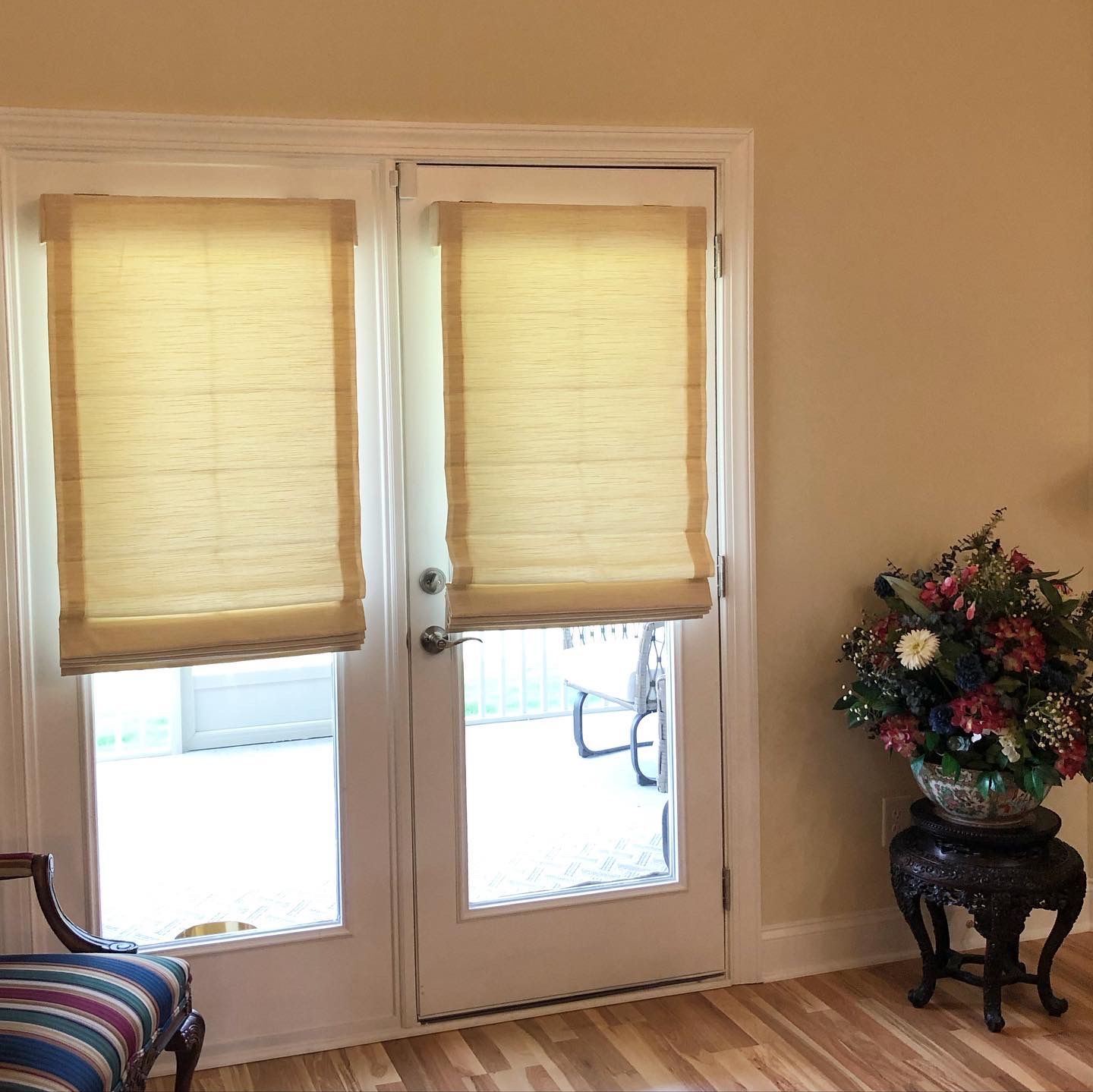 Two French doors with tan shades, a floral arrangement, and a striped chair in a room with hardwood floors.