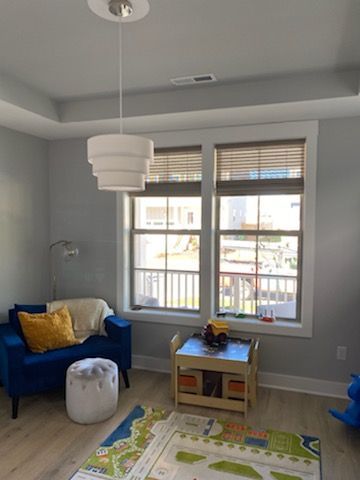 Blue chair and play table in a light-blue room with layered pendant light and window with blinds.