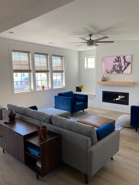 Living room with gray sofa, blue chairs, fireplace, and windows with wood blinds.