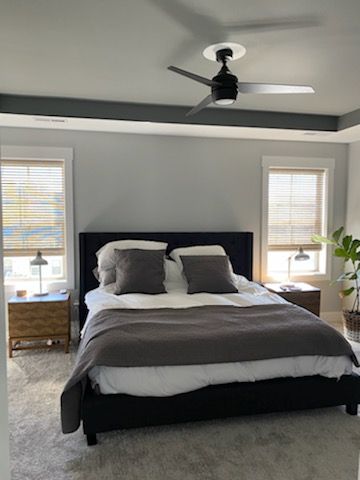 Bedroom with a bed, nightstands, windows, ceiling fan, and potted plant. Gray and white color scheme.