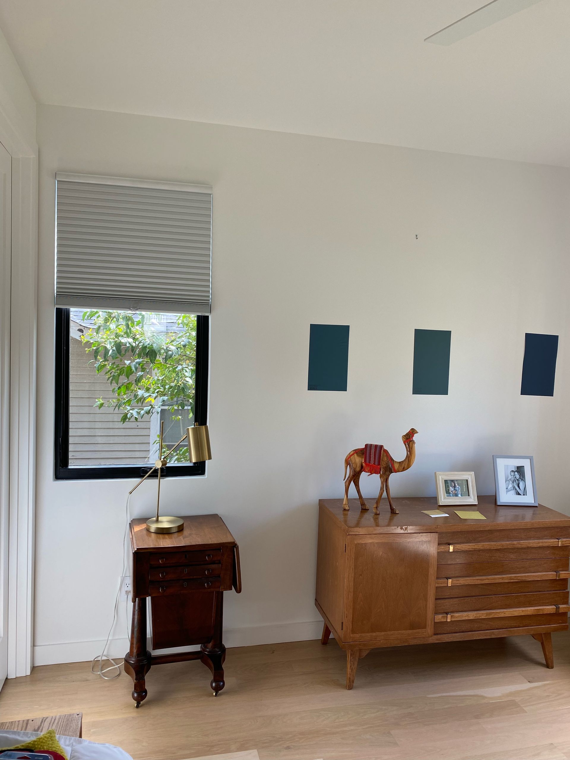 Bedroom with a window, dresser, table, and paint swatches on the wall. Camel statue on the dresser.