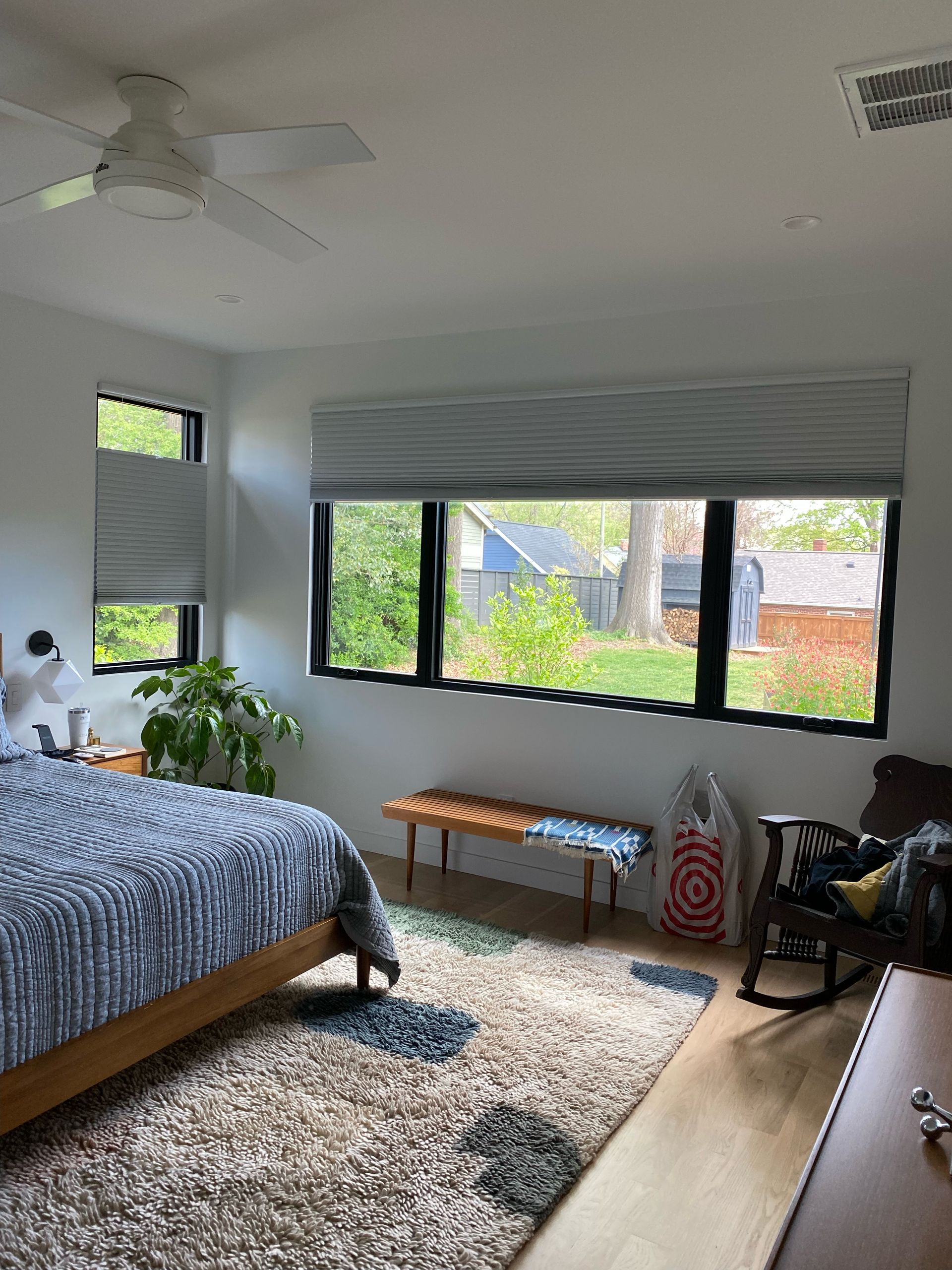 Bedroom with bed, bench, rug, windows with shades, and ceiling fan.