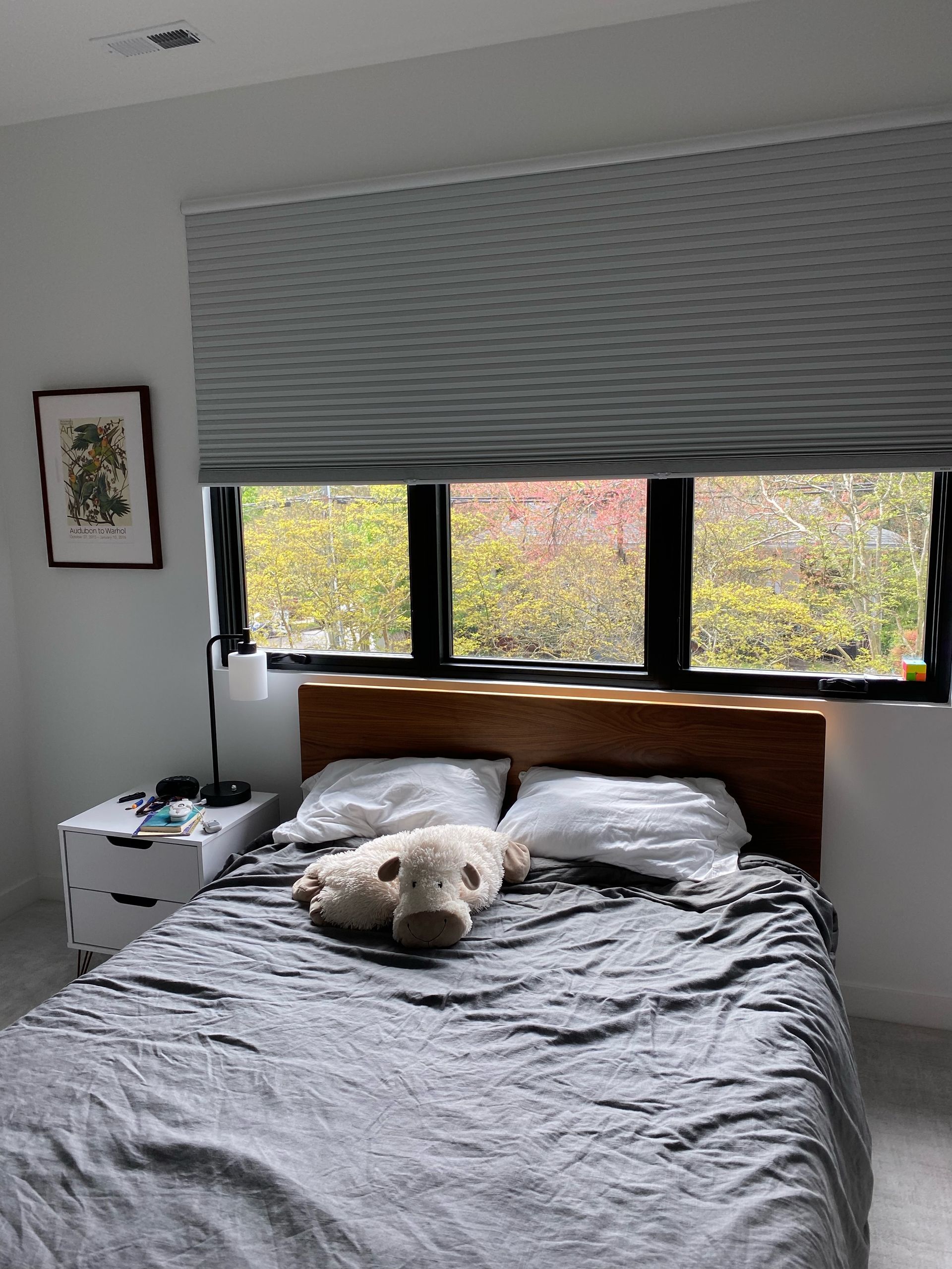 Bedroom with bed, window, blinds, nightstand, framed artwork, and plush animal.