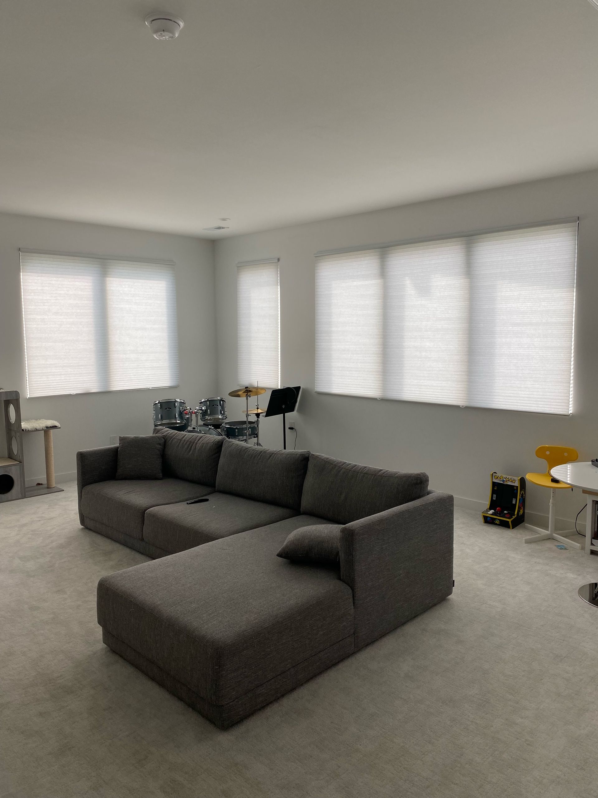 Gray sectional sofa in a room with white walls, three windows, and light gray carpet.