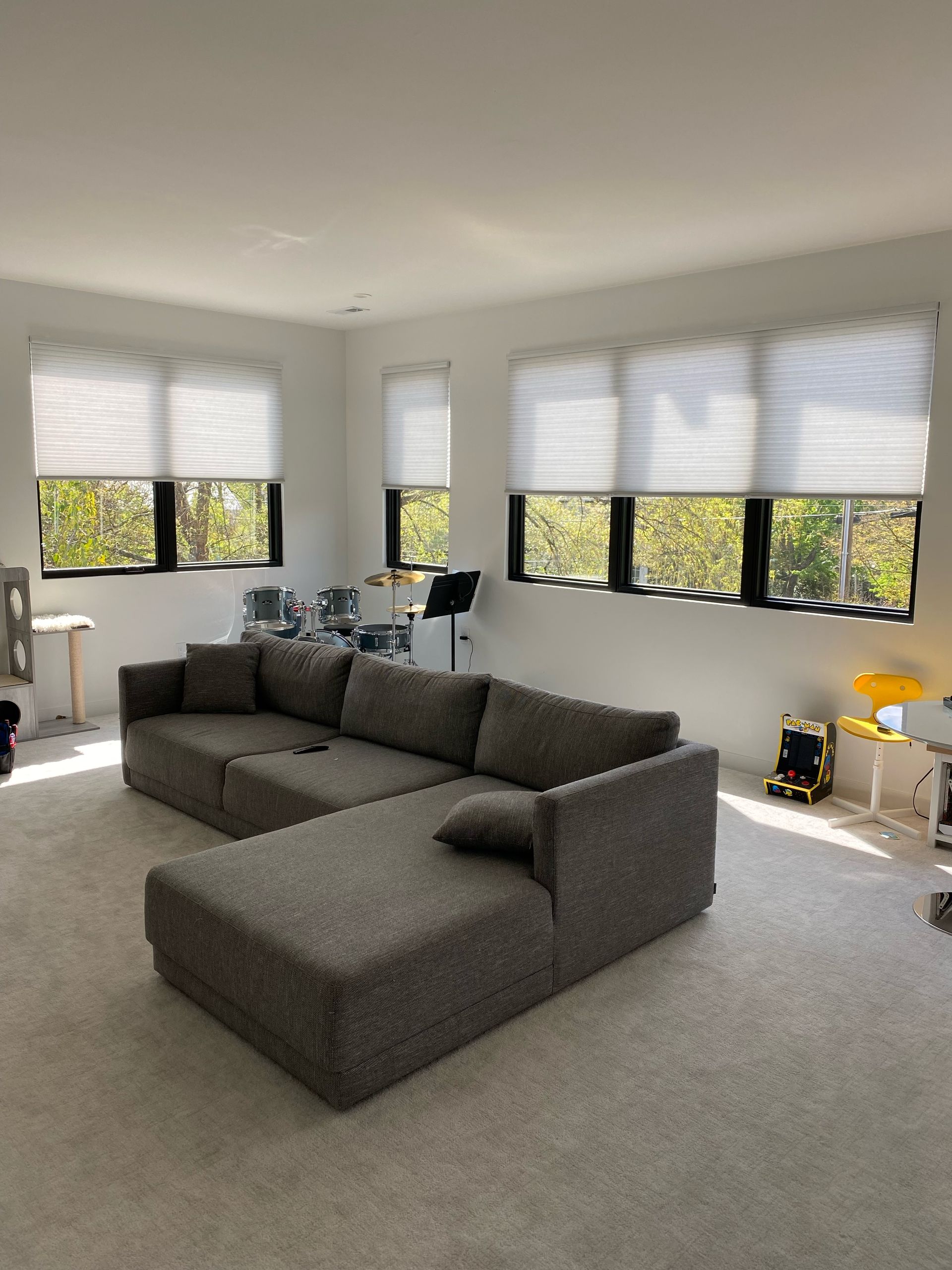 Gray sectional sofa in a bright room with light-colored blinds and a window overlooking trees.