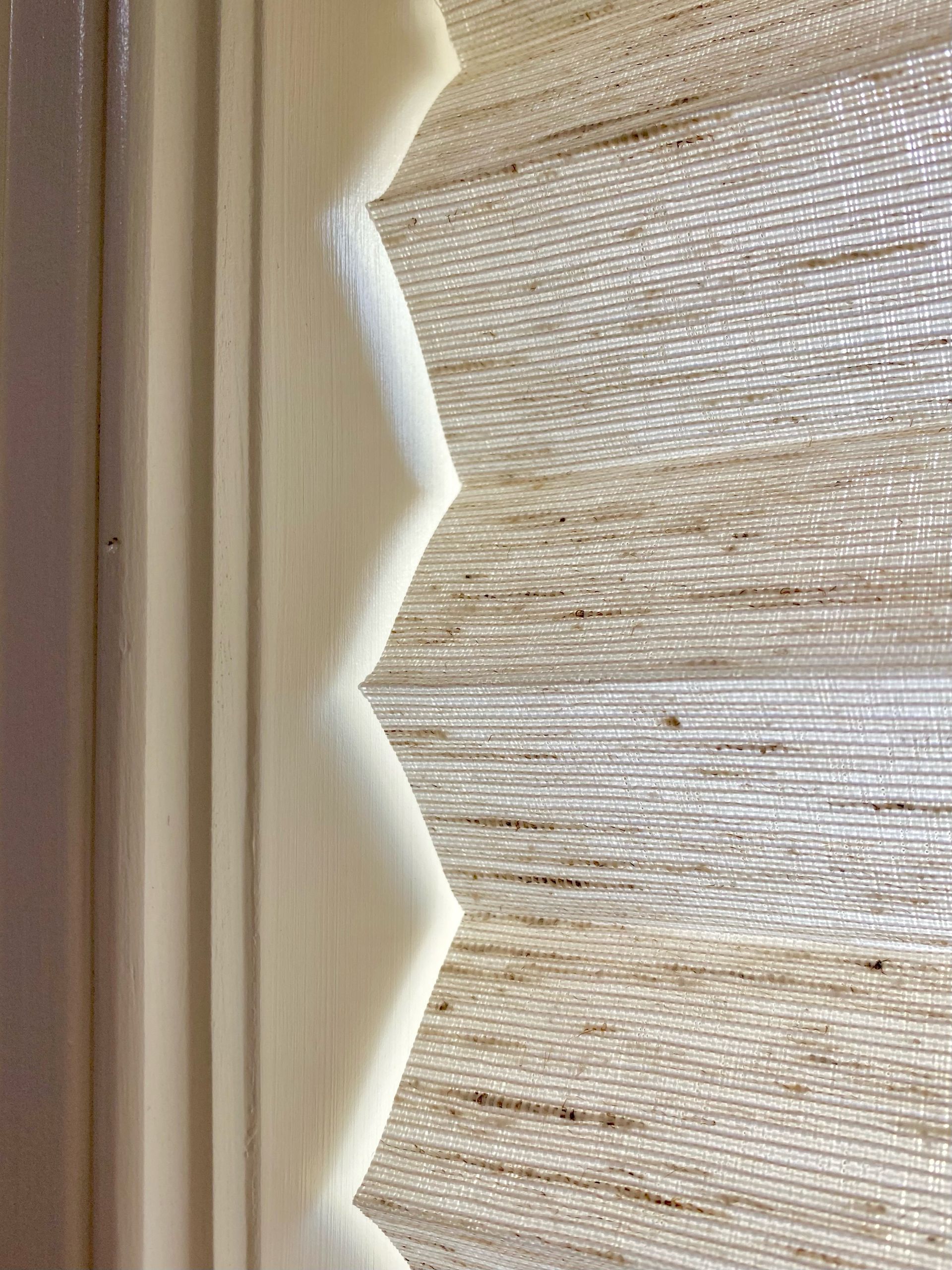 Cream-colored window trim and zig-zag edged shade, tan woven fabric, side view.