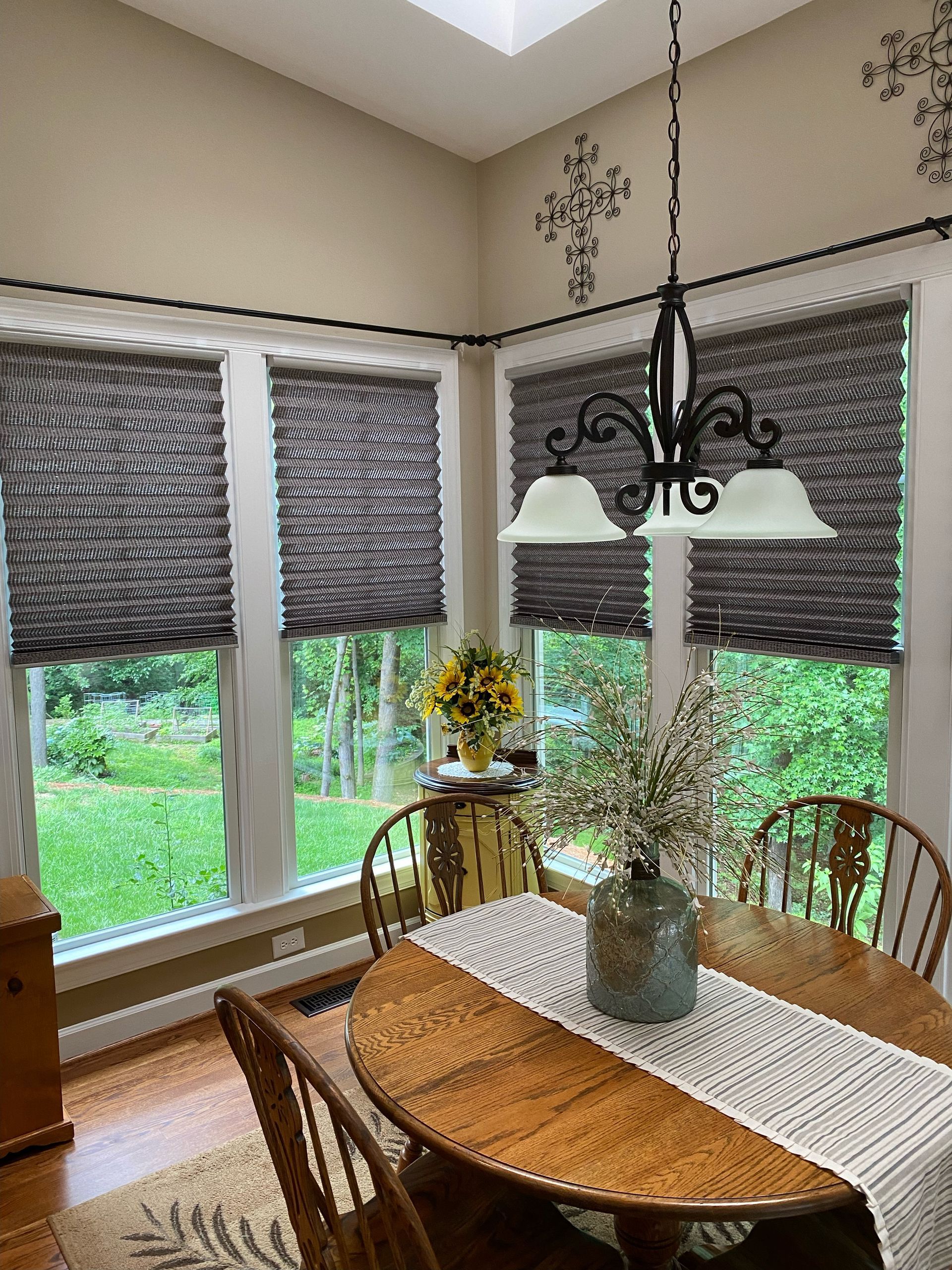 Dining room with dark gray woven shades, a round wooden table, and a chandelier.
