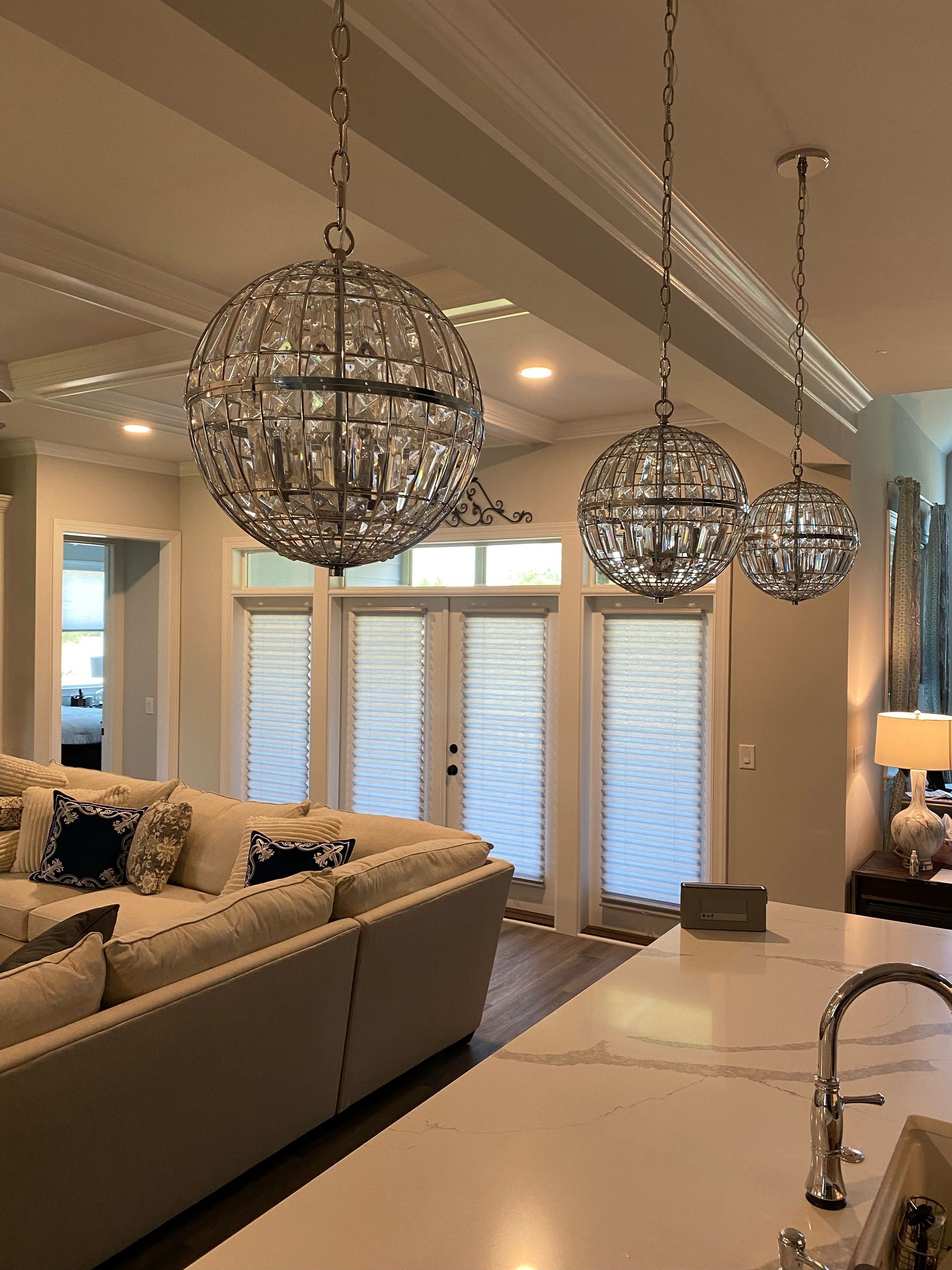 Three crystal orb chandeliers hang above a kitchen island, with a sofa and patio doors in the background.