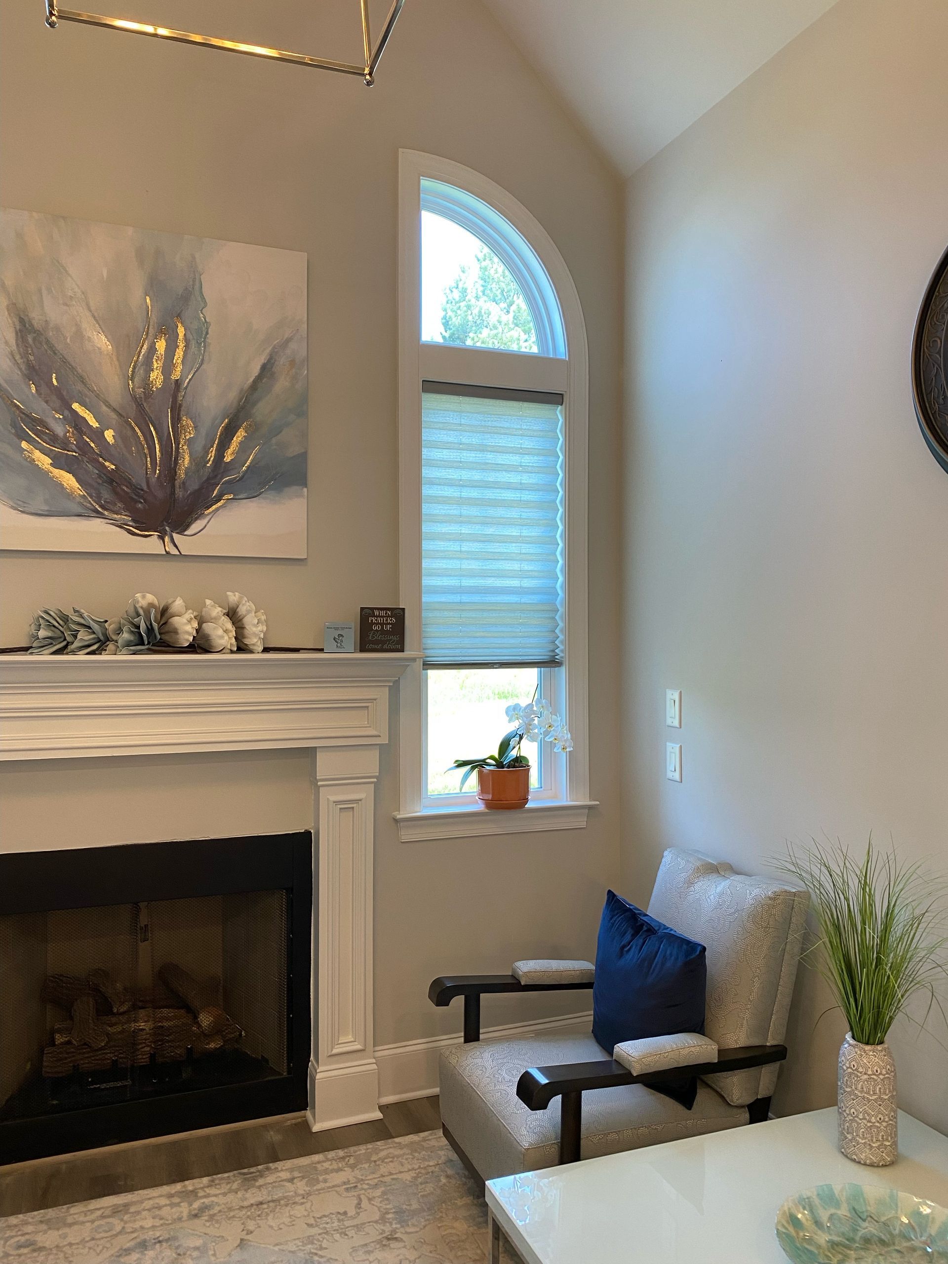 Living room with fireplace, arched window, armchair, artwork. Neutral tones, blue accents.