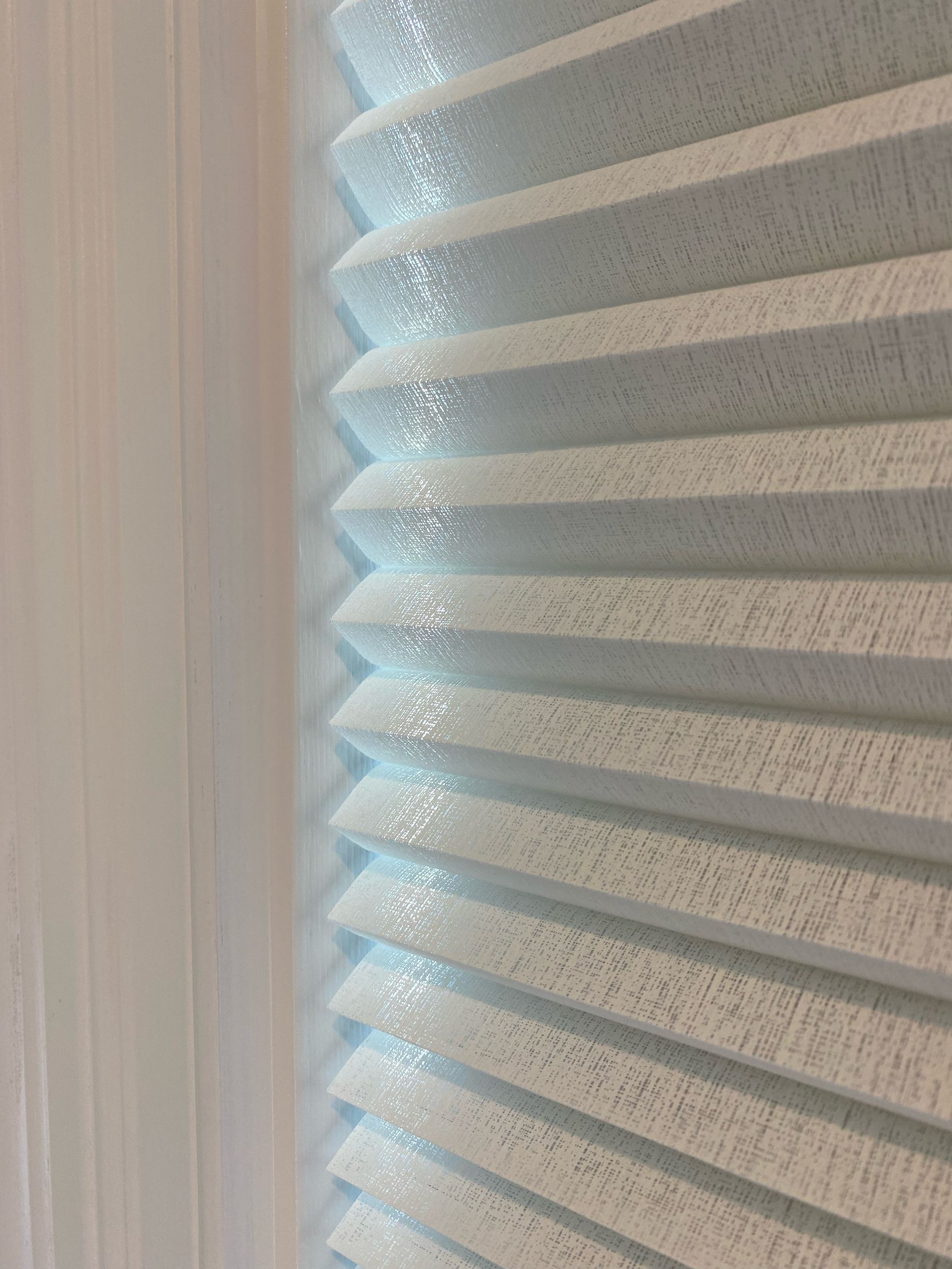Light blue pleated window blinds are next to a white curtain.