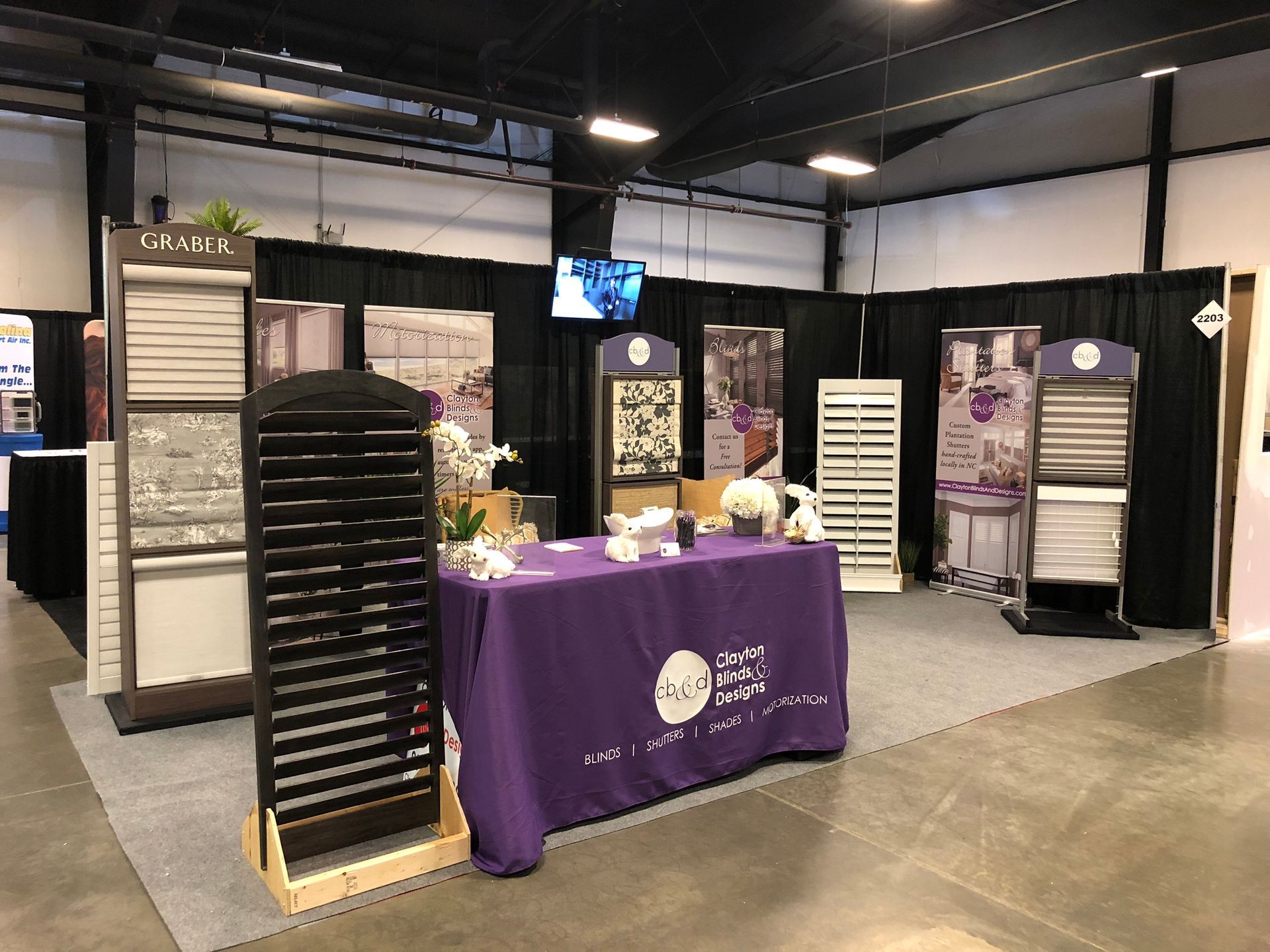 Trade show booth with window treatment displays and purple table cloth.