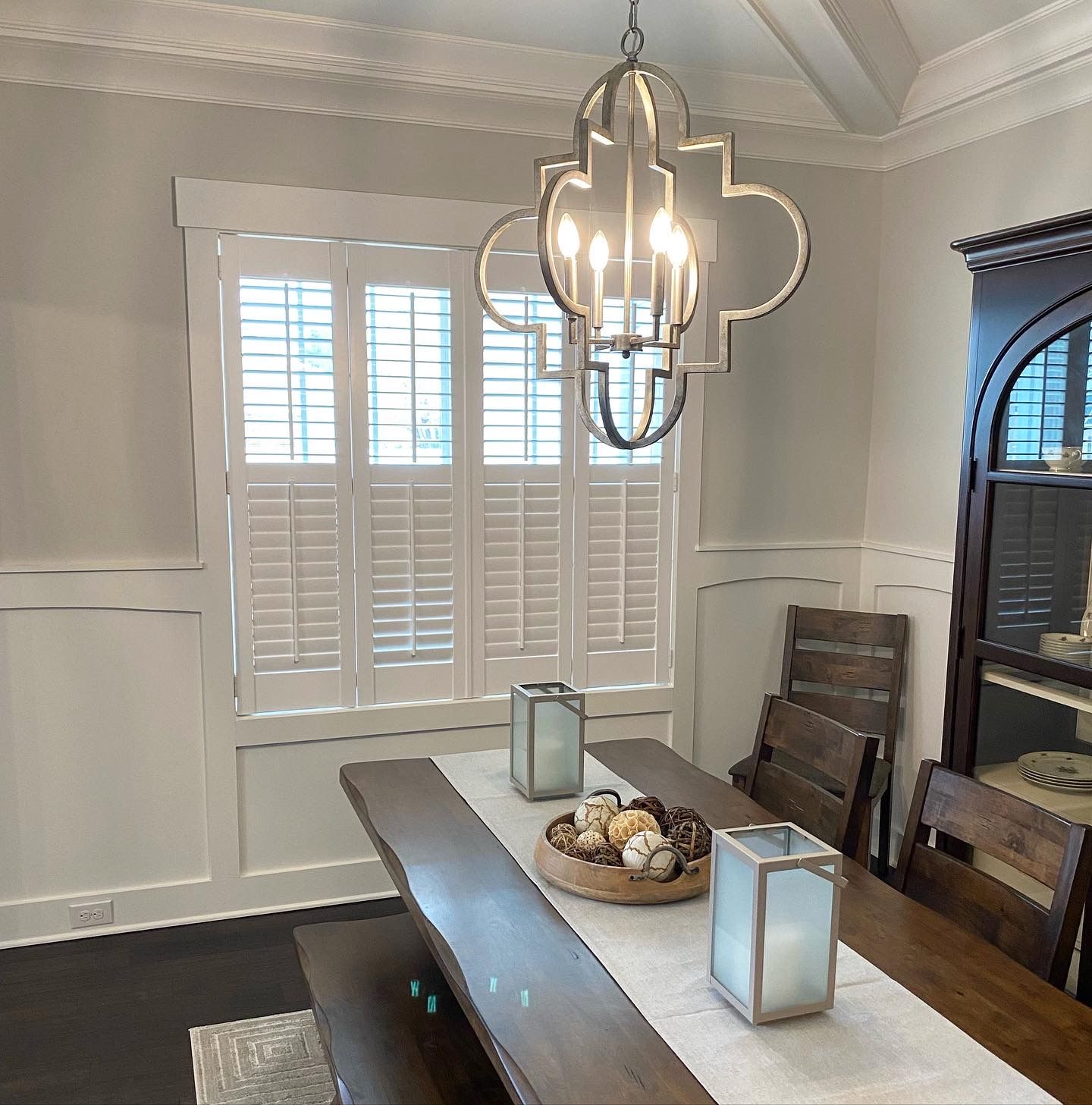 Dining room with wooden table, shutters, and decorative chandelier.