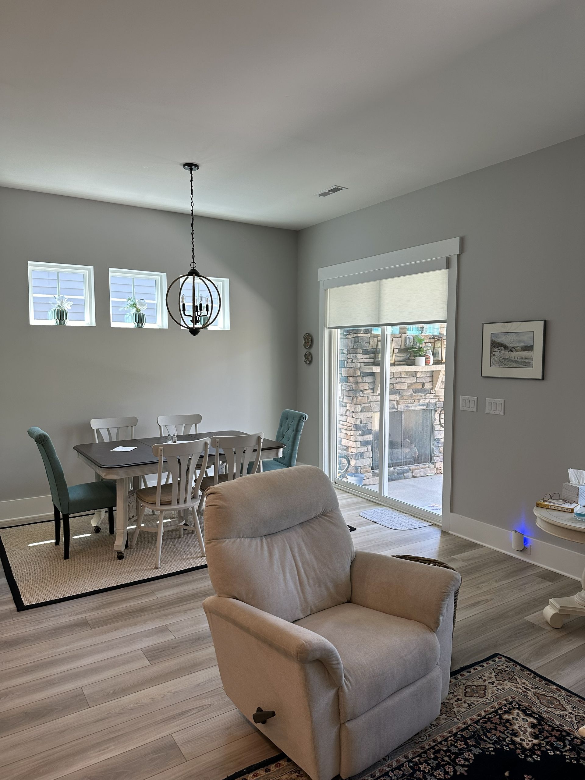 Living room with dining table, recliner, and sliding glass door. Gray walls and light wood floors.