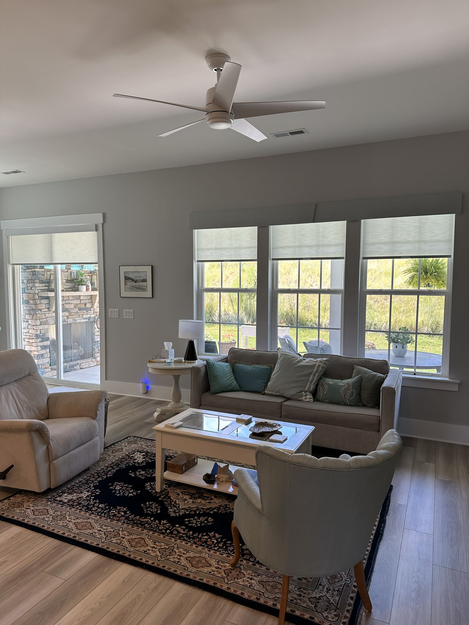 Living room with sofa, chairs, rug, windows, and ceiling fan.