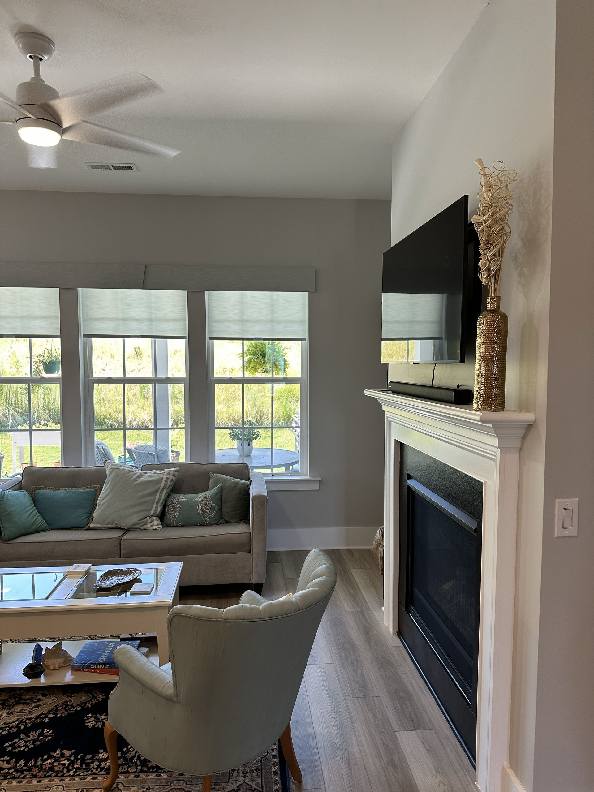 Living room with sofa, chair, fireplace with TV, windows, and ceiling fan.
