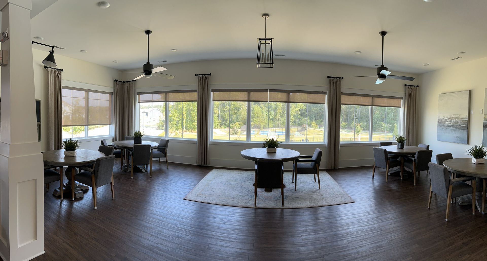 Spacious dining area with round tables, chairs, large windows, and three ceiling fans; natural light and neutral color palette.