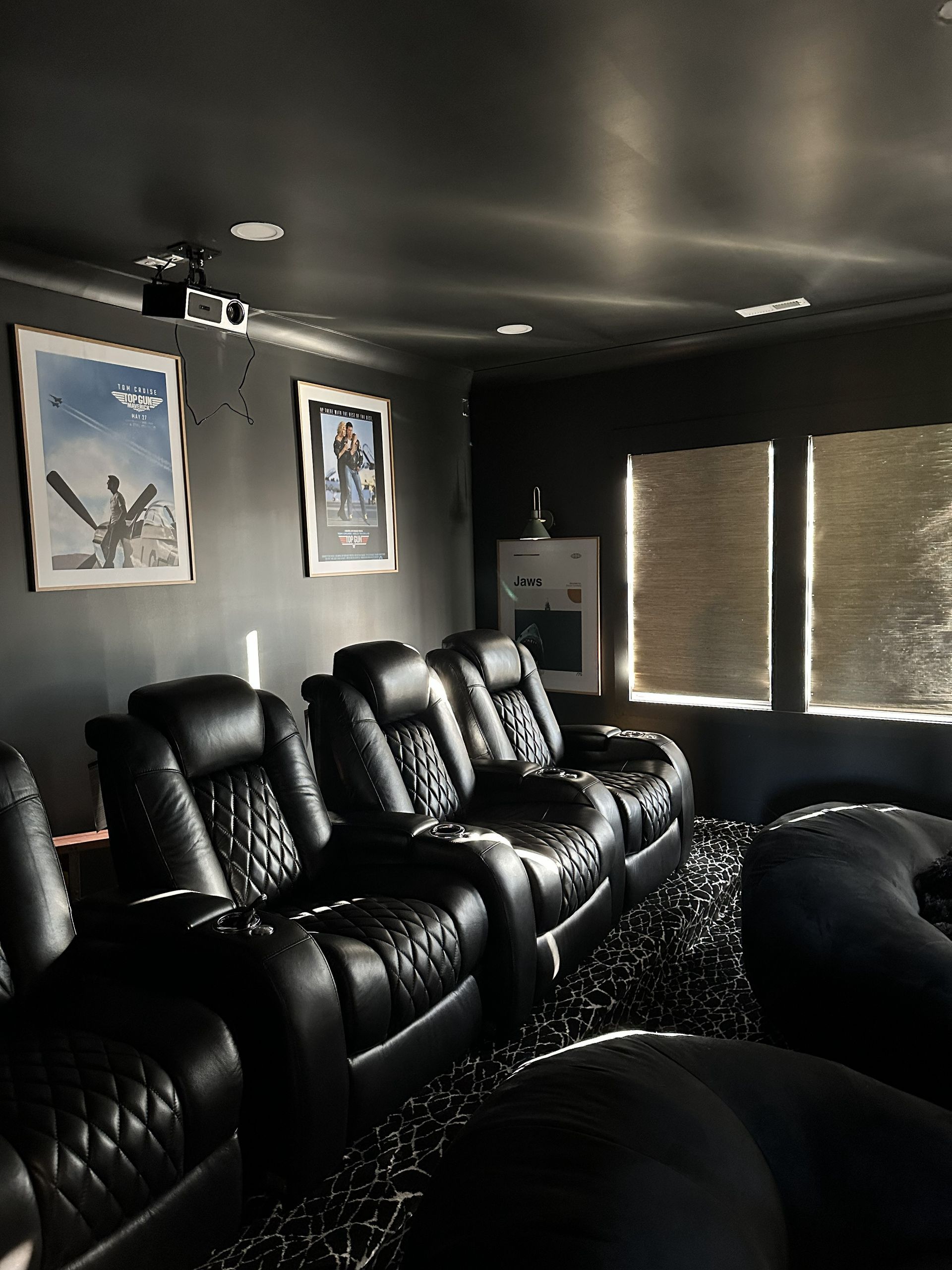 Home theater with black leather recliners, dark walls, Star Wars art, and window shades.