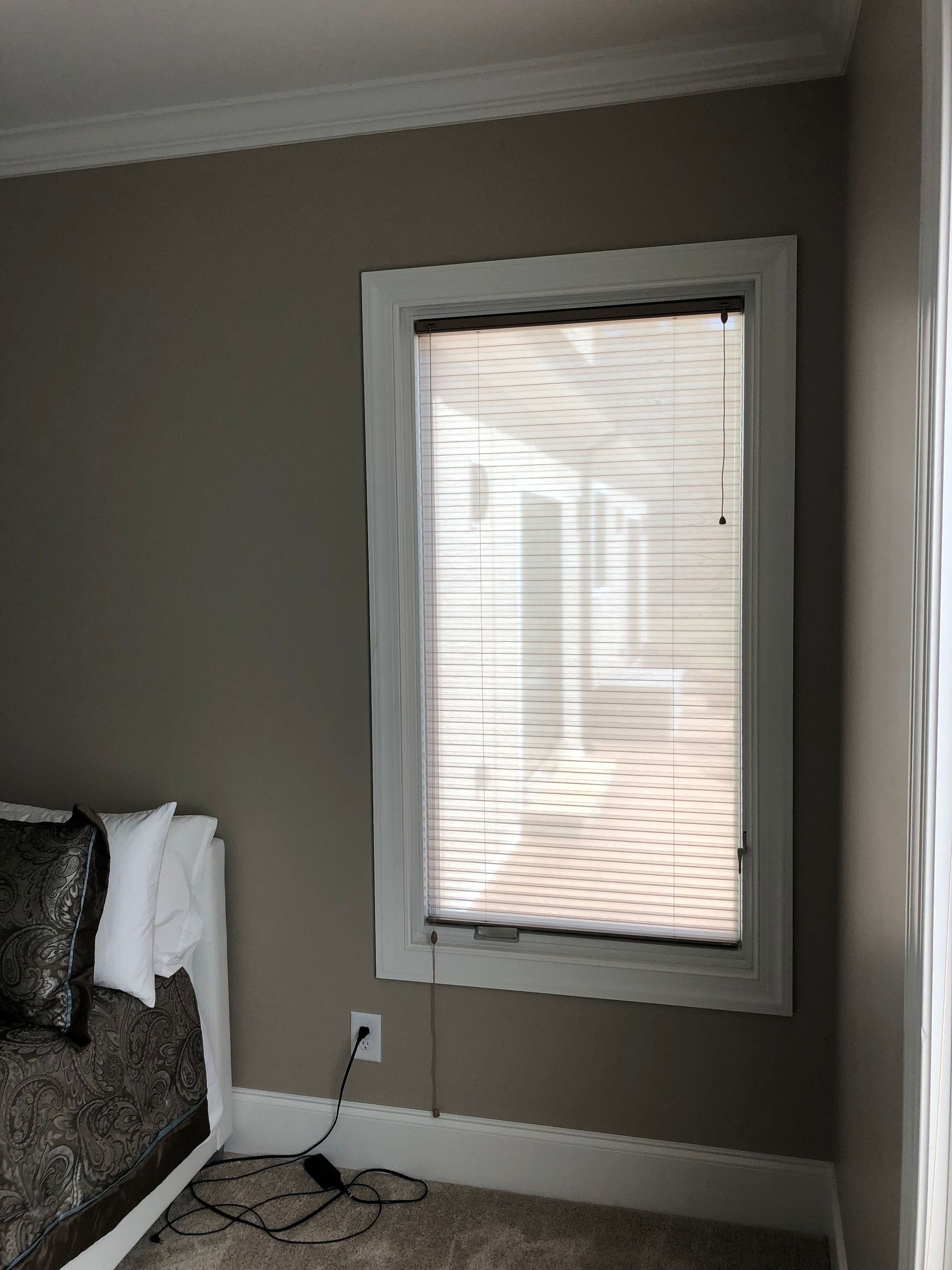 Window with closed blinds, white trim, and a cord hanging down, against a tan wall.