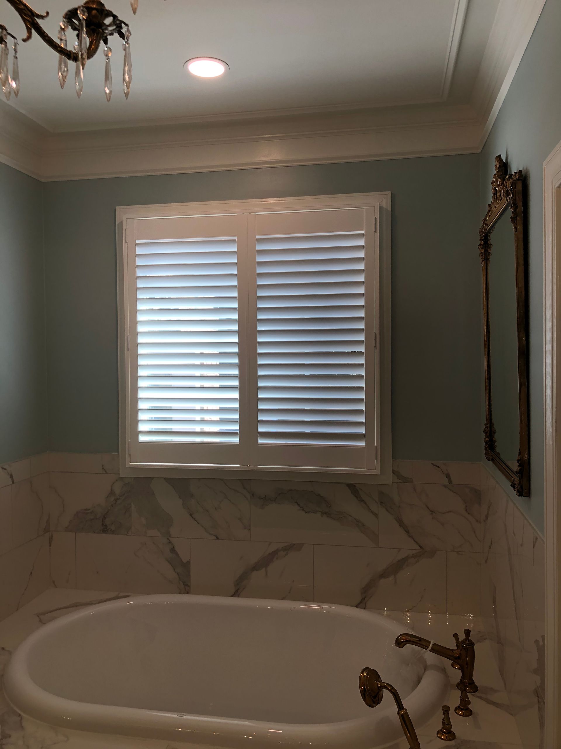 Bathroom with white shutters, a bathtub, and marble walls.