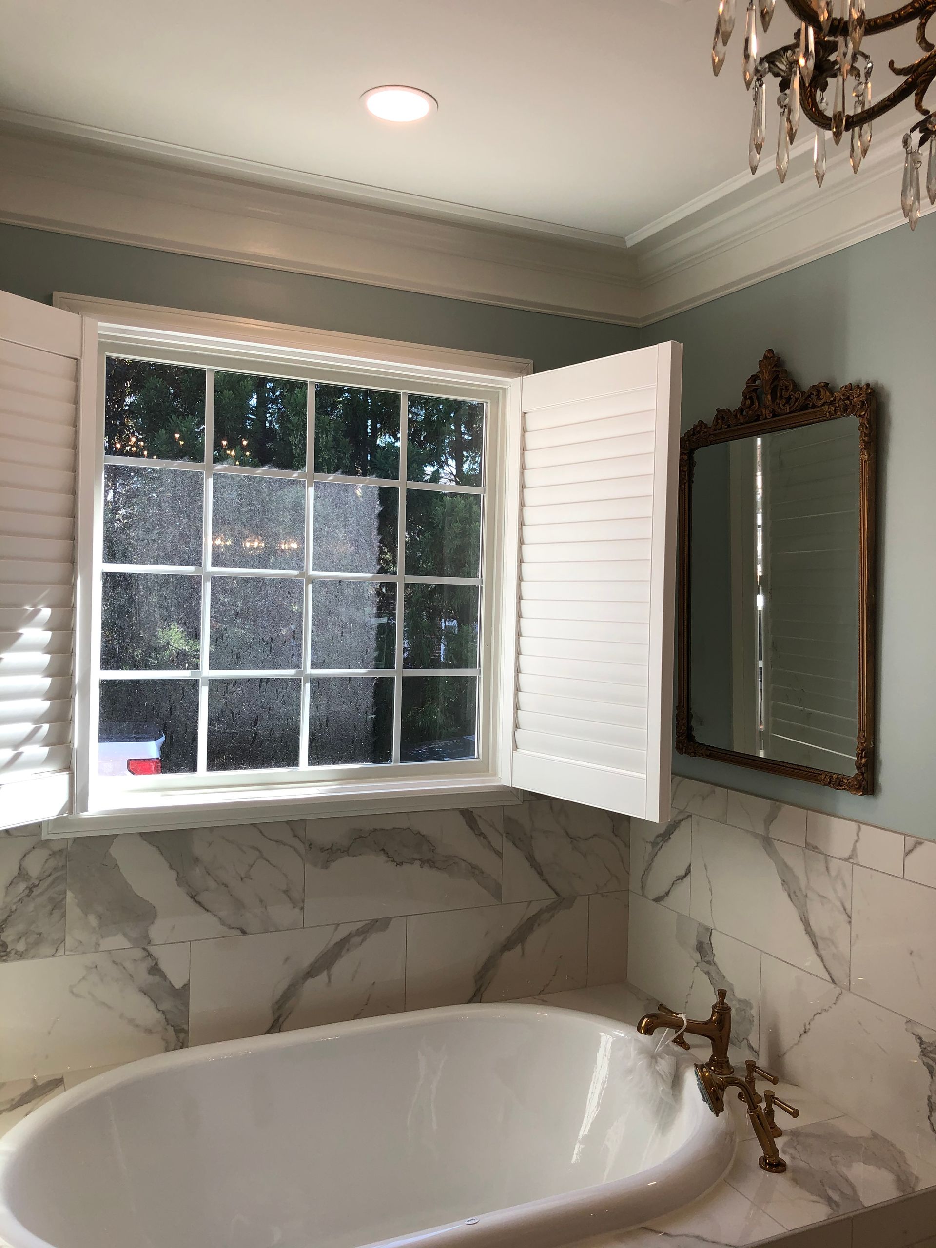 Bathroom with a white bathtub, marble surround, and window with open white shutters.