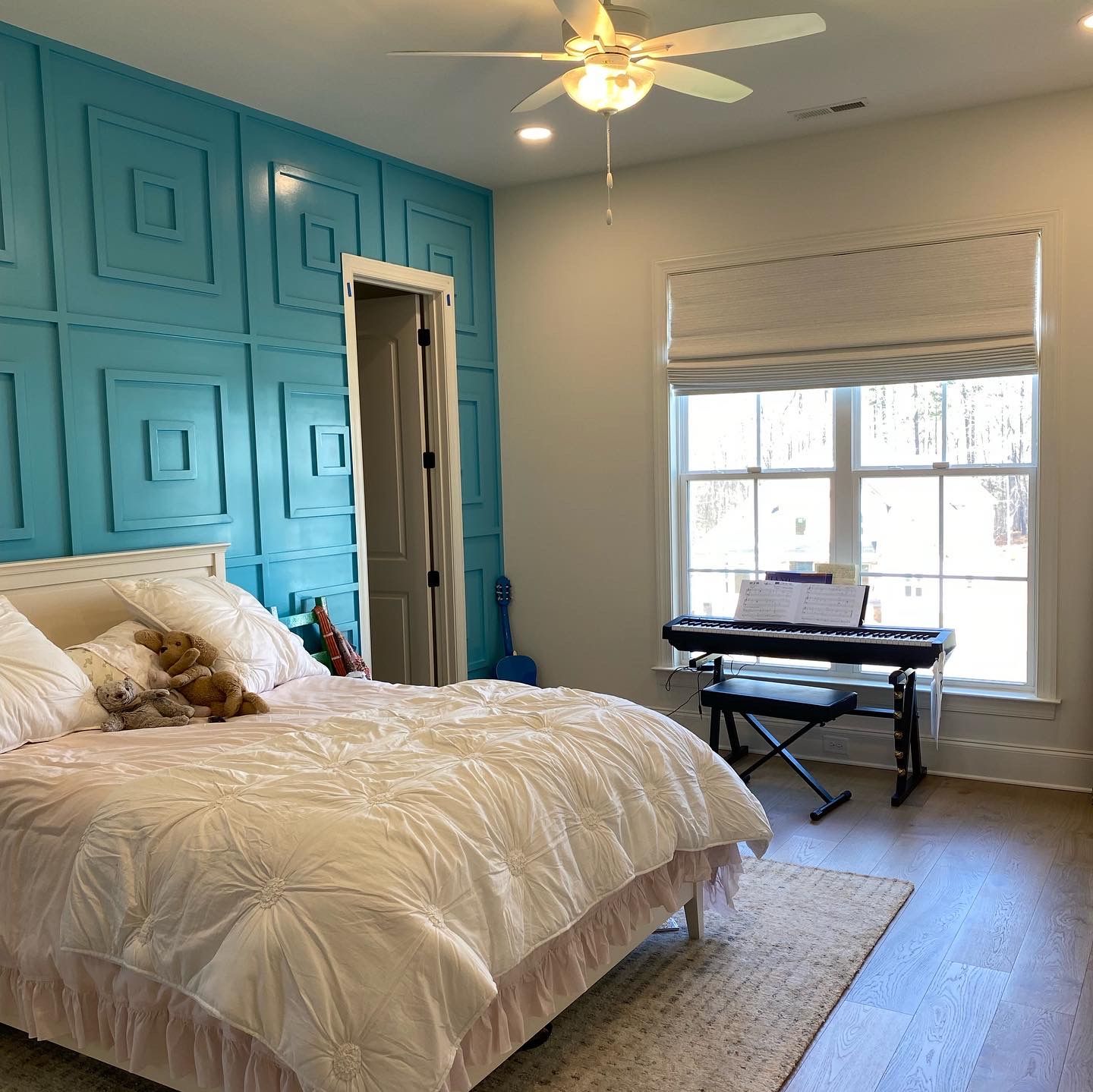 Bedroom with turquoise accent wall, bed, keyboard, window, and rug.