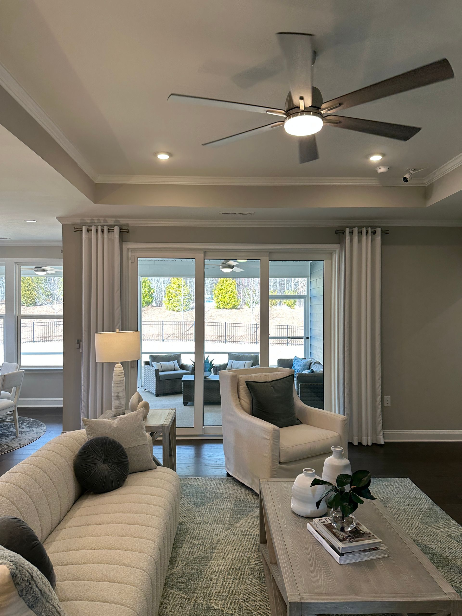 Living room with couch, armchair, rug, sliding glass door leading to outdoor seating area. Ceiling fan.