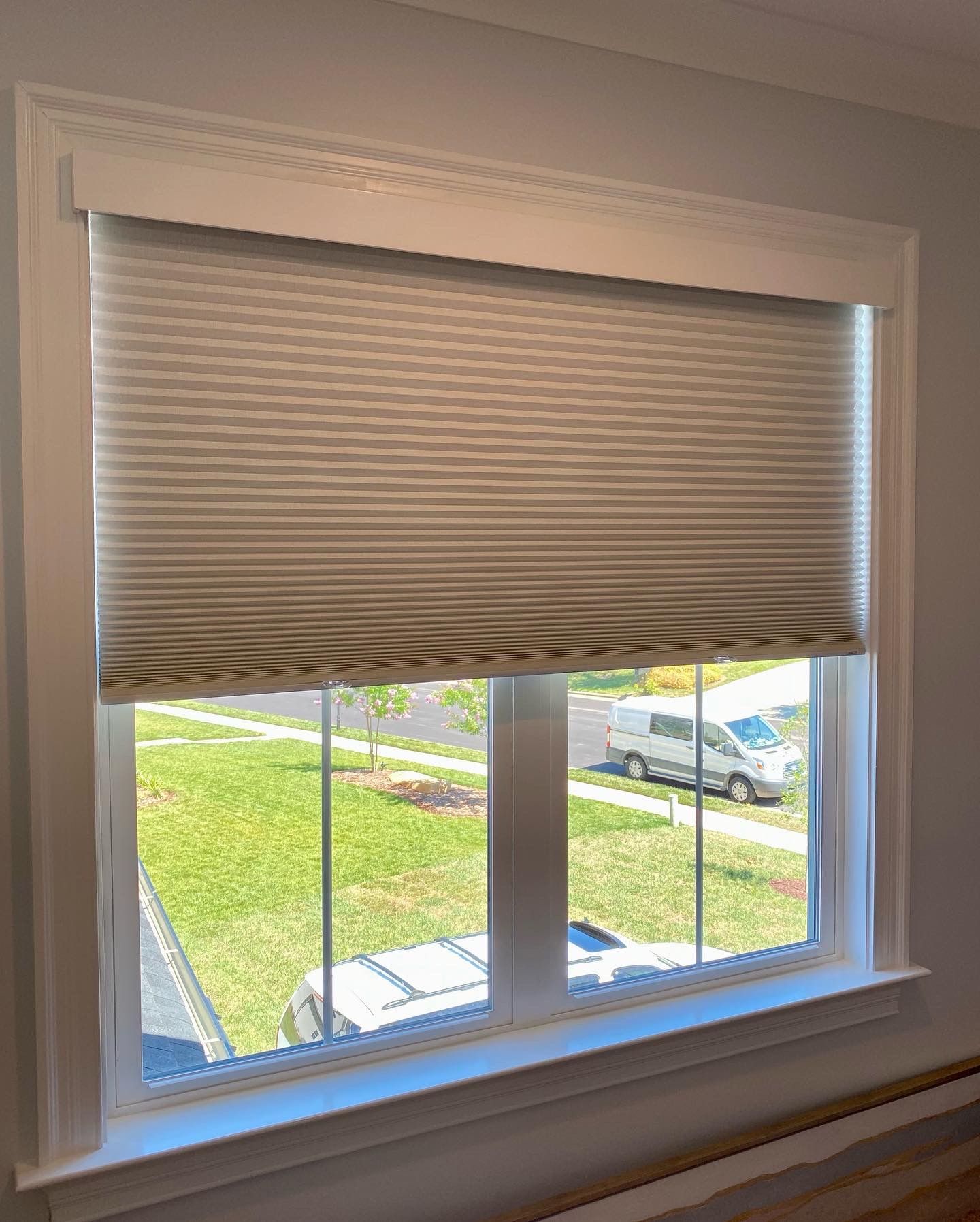 Window with light gray pleated shade; view of green lawn and white van outside.
