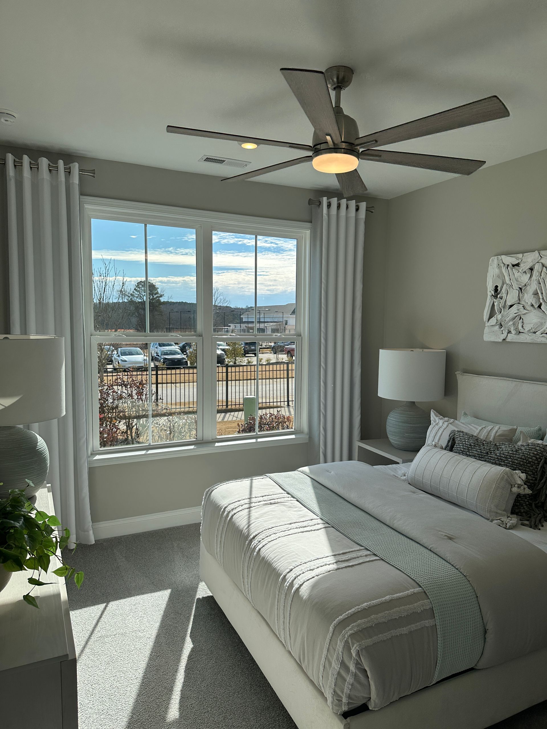 Bedroom with large window, white bedding, gray walls, ceiling fan, and light blue accents.