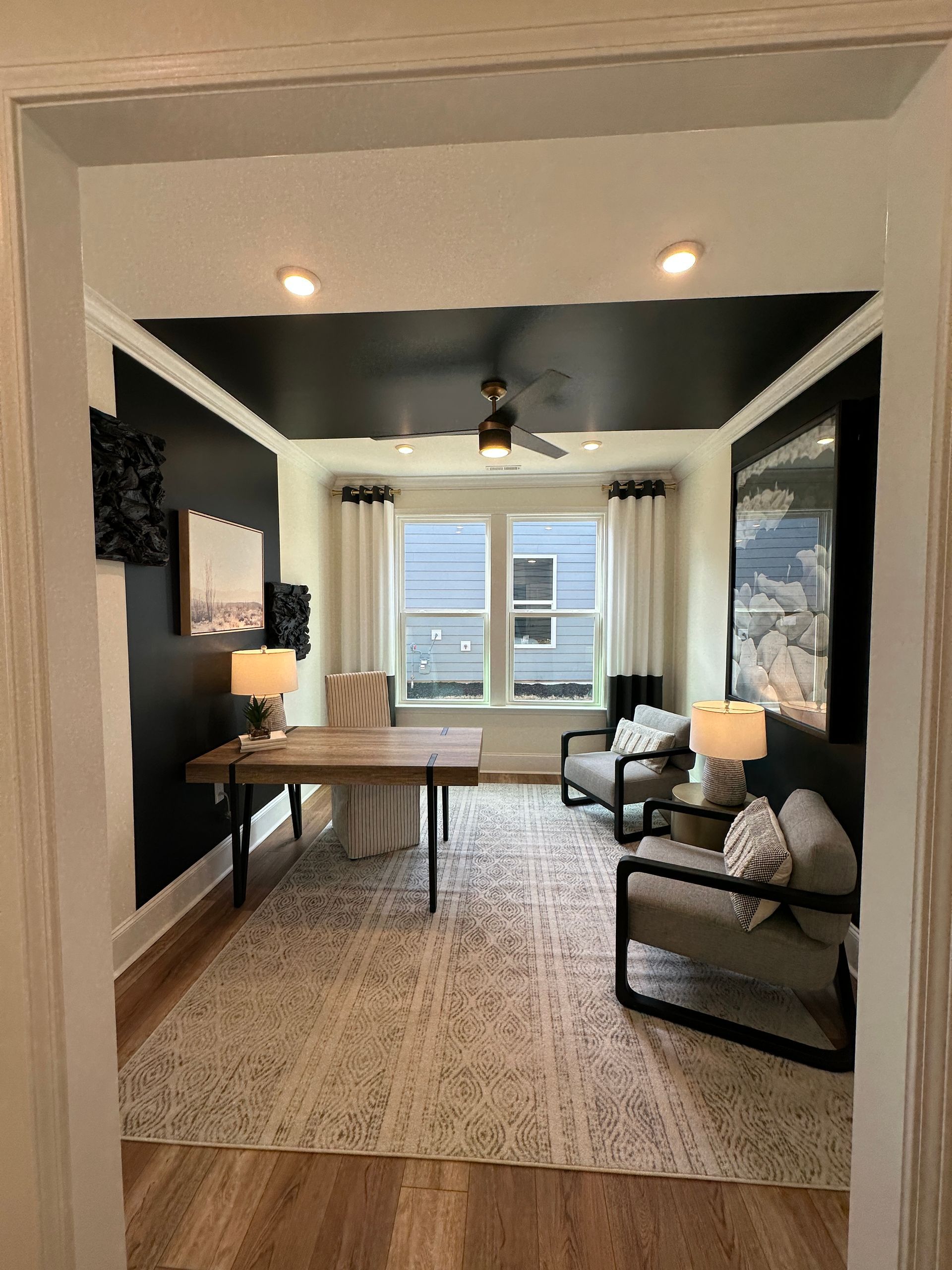 Home office with black ceiling and accent walls, desk, armchairs, rug, and window.