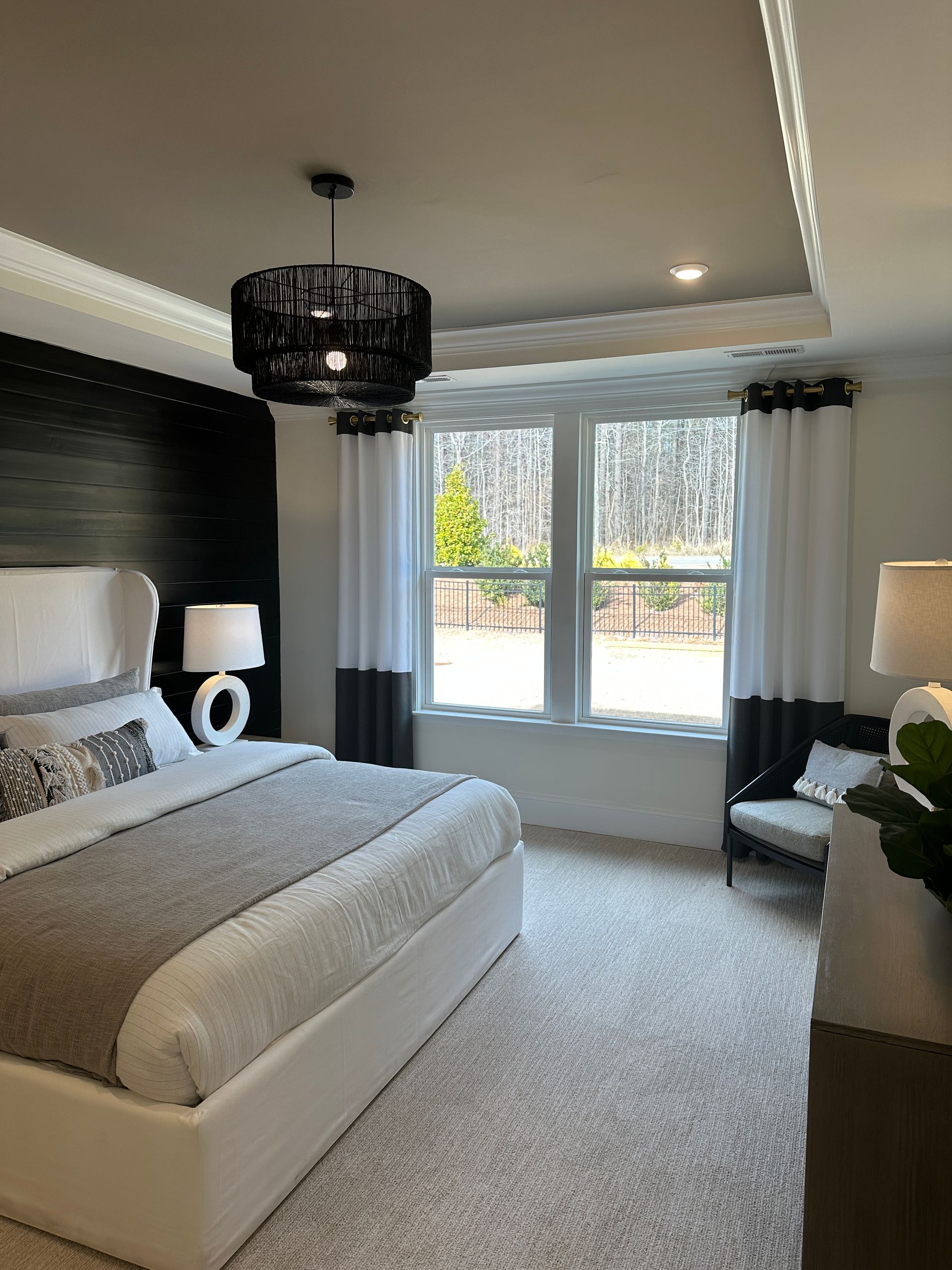 Bedroom with bed, lamp, and window, neutral tones, black accent wall.