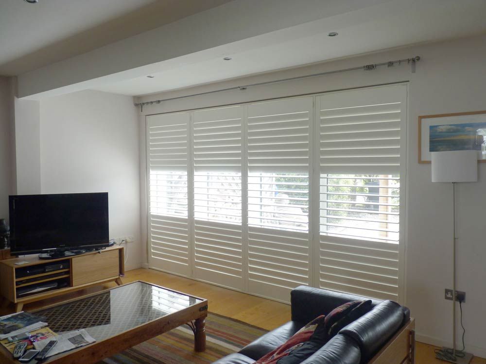 Living room with white shutters covering a large window. A TV, couch, and coffee table are visible.