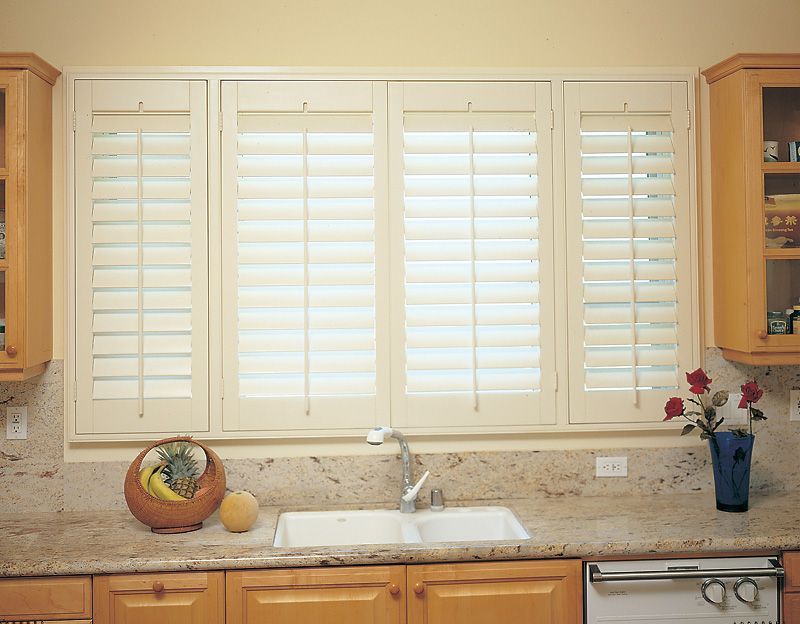 Kitchen window with white shutters above a sink and granite countertop.