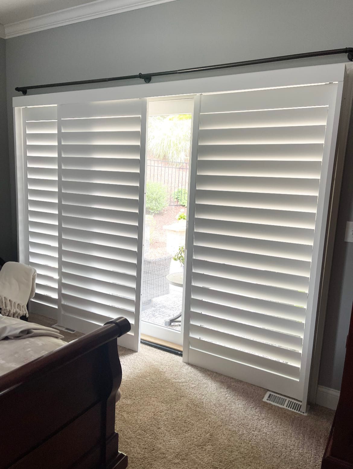 White shutters partially open over sliding glass door, in a bedroom with brown carpet.