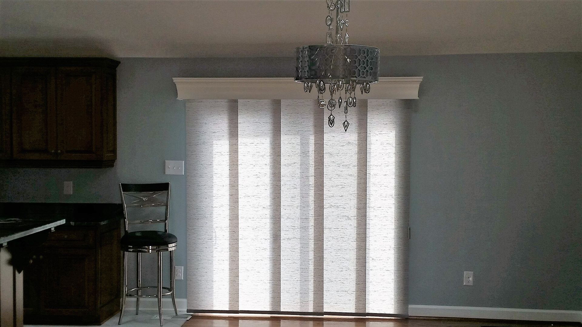 Kitchen with a chandelier, panel blinds, dark cabinets, and a bar stool.