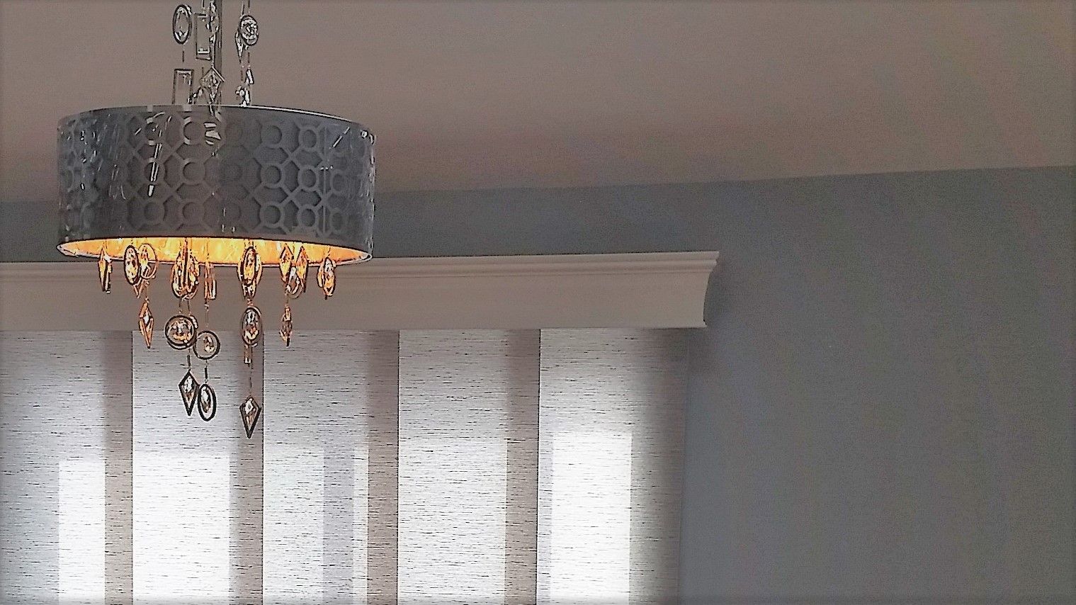 Chandelier hanging above vertical blinds against a light blue wall.